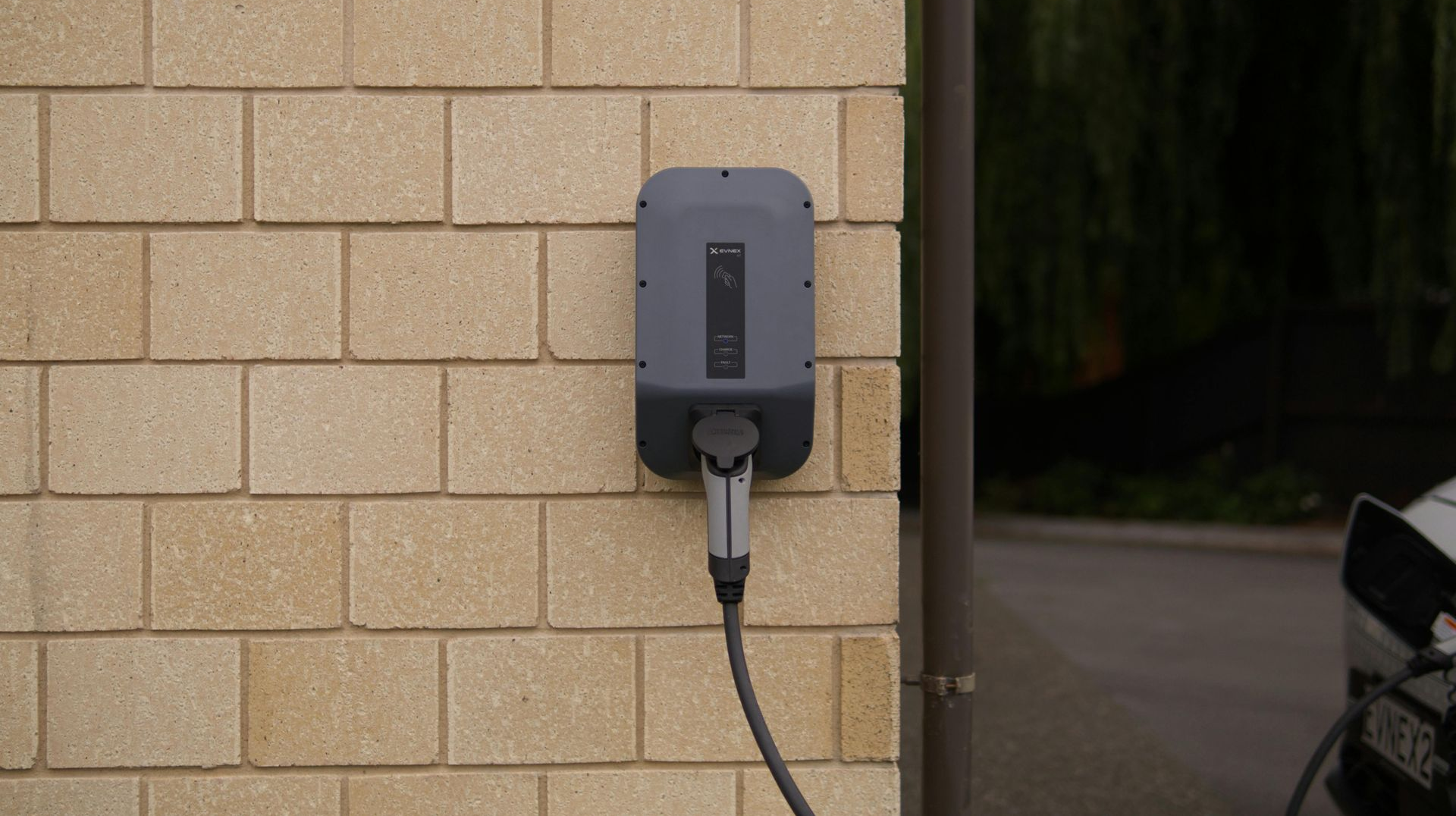 Electric vehicle charger mounted on a beige brick wall with charging cable plugged in.