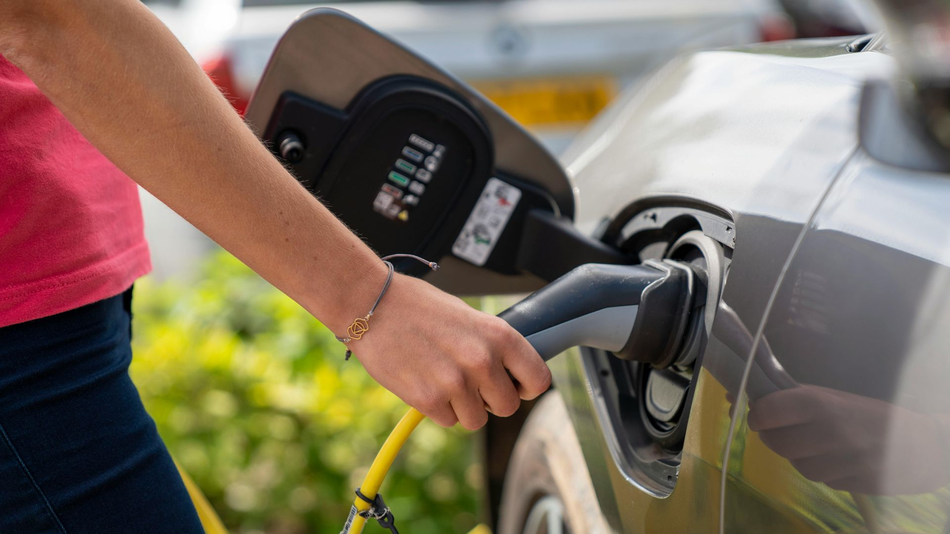 Person plugging a gray electric vehicle with a yellow charging cable.