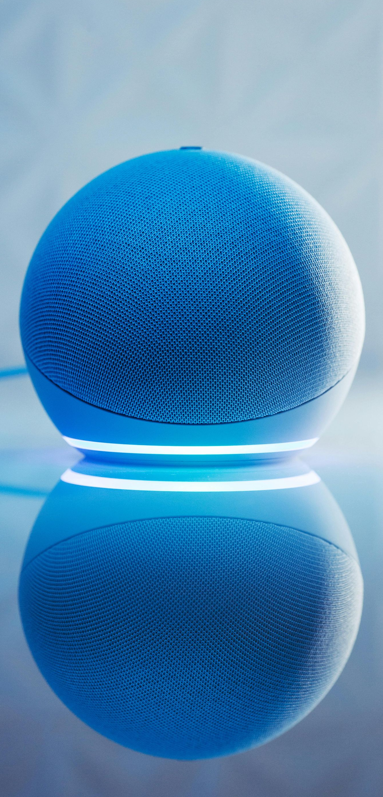 Blue spherical smart speaker with glowing base reflected on a shiny surface.