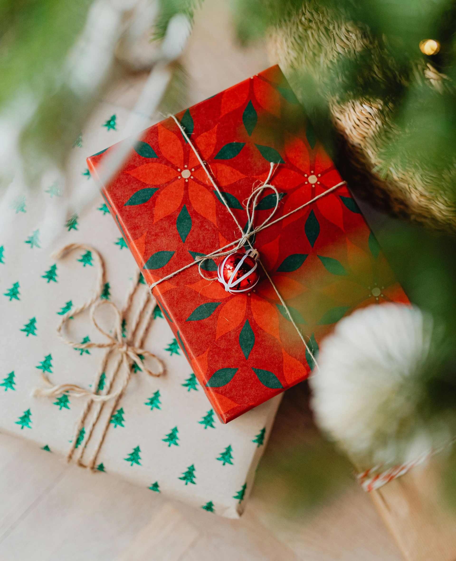 Wrapped Christmas gifts: red poinsettia and green tree paper, tied with twine, near a Christmas tree.