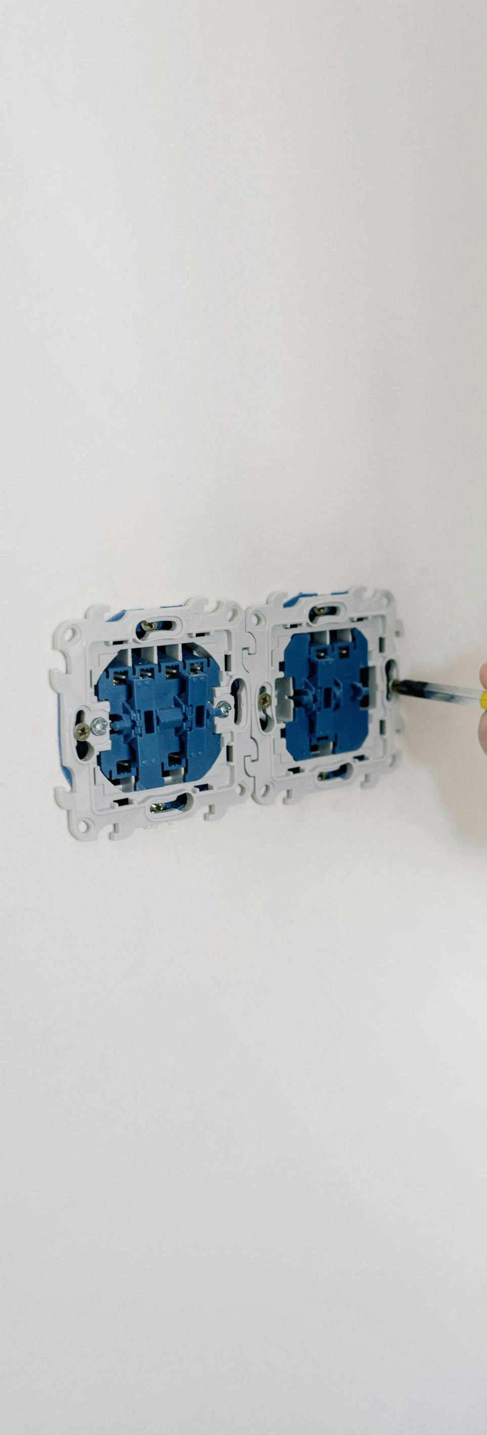 A person uses a screwdriver to mount two electrical socket wall boxes onto a white wall.