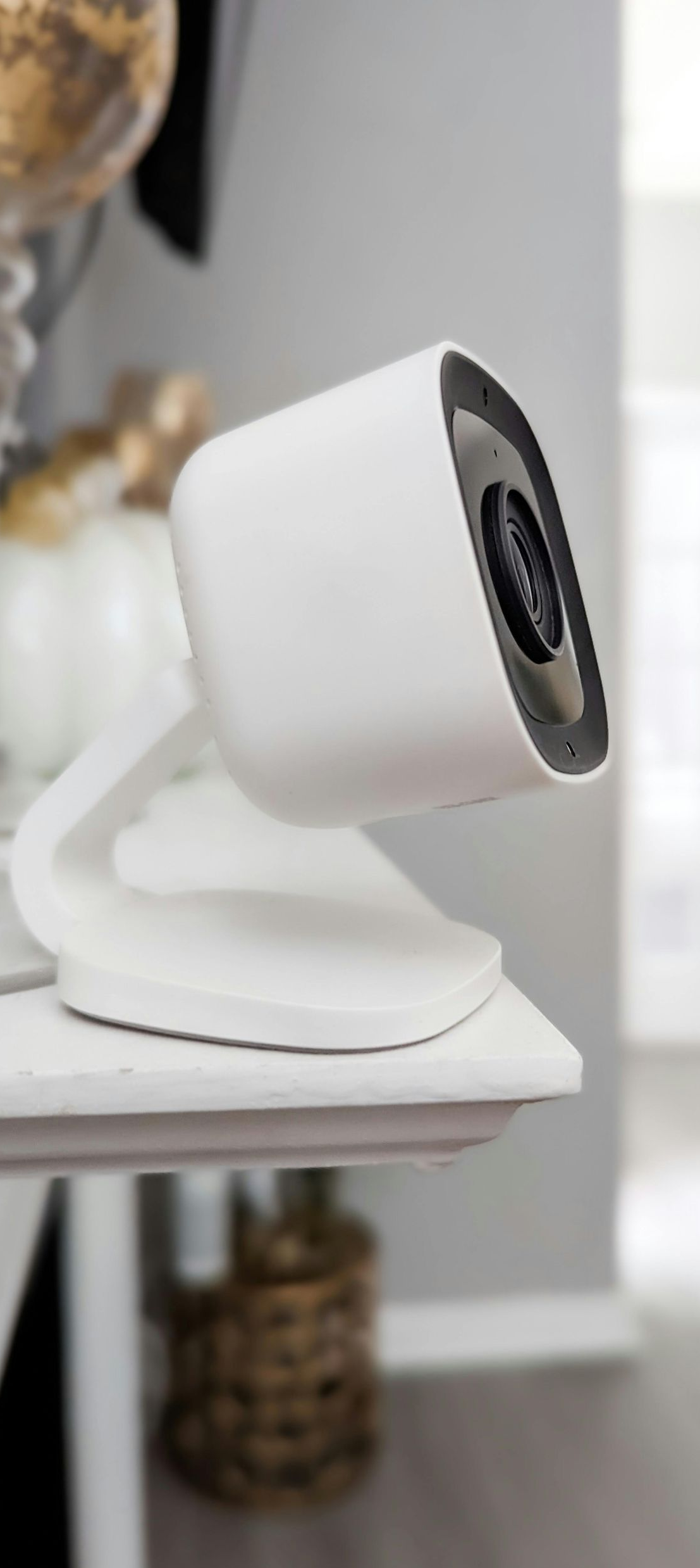 White security camera on a shelf, facing forward, gray background.