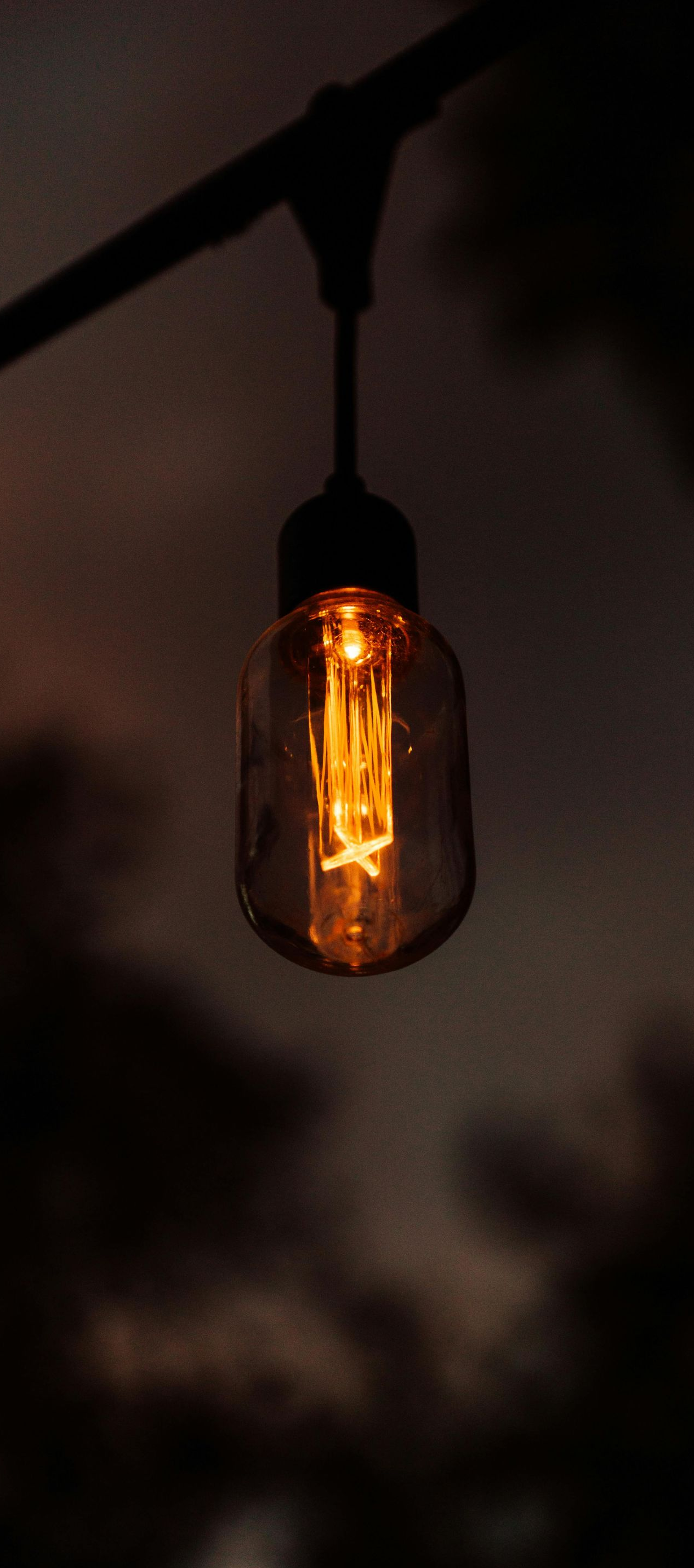Lit Edison bulb hanging from a black wire, orange glow against a dark sky.