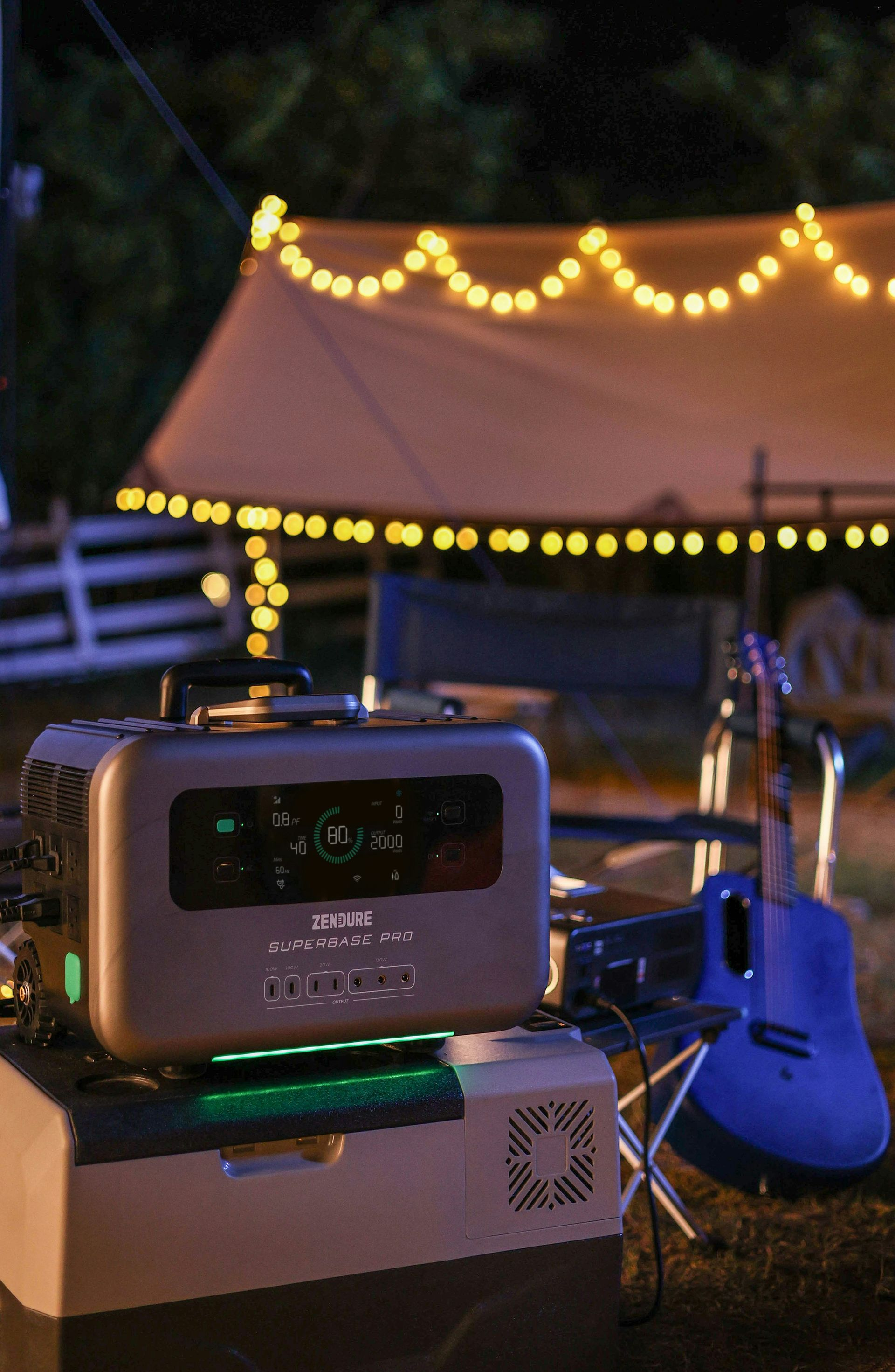 Camping scene: portable power station on cooler, guitar, string lights, tent in the background at night.