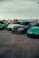 Row of sports cars parked on pavement under a cloudy sky, with people in the background