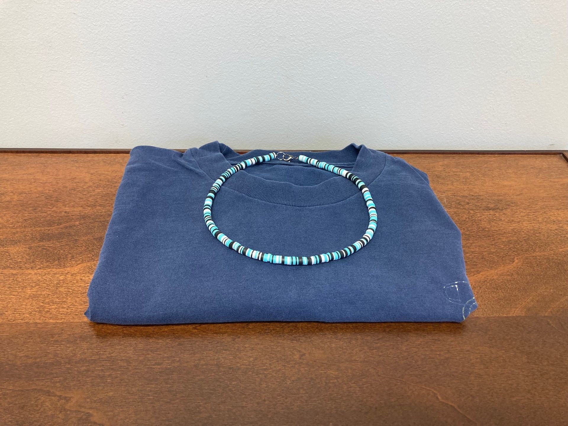 Folded blue shirt with a turquoise beaded necklace on a wooden table