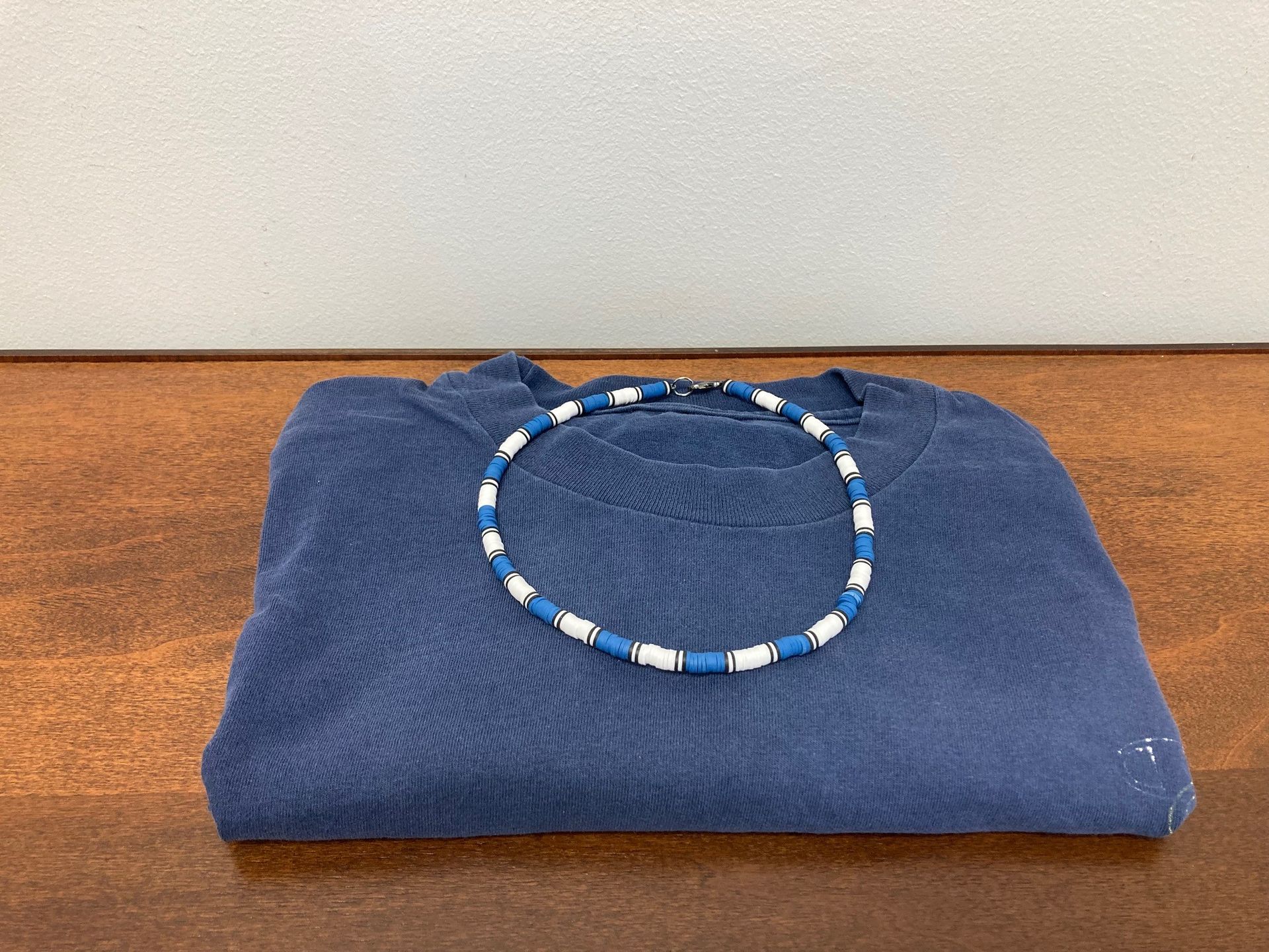 Folded blue sweater with a blue-and-white beaded necklace on top.