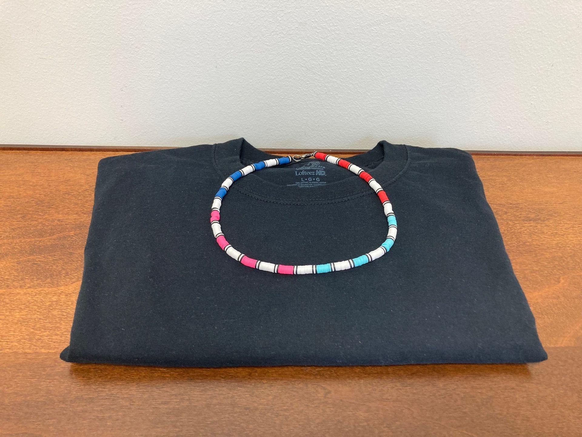 Folded dark sweater with a colorful beaded bracelet on top, resting on a wooden surface.