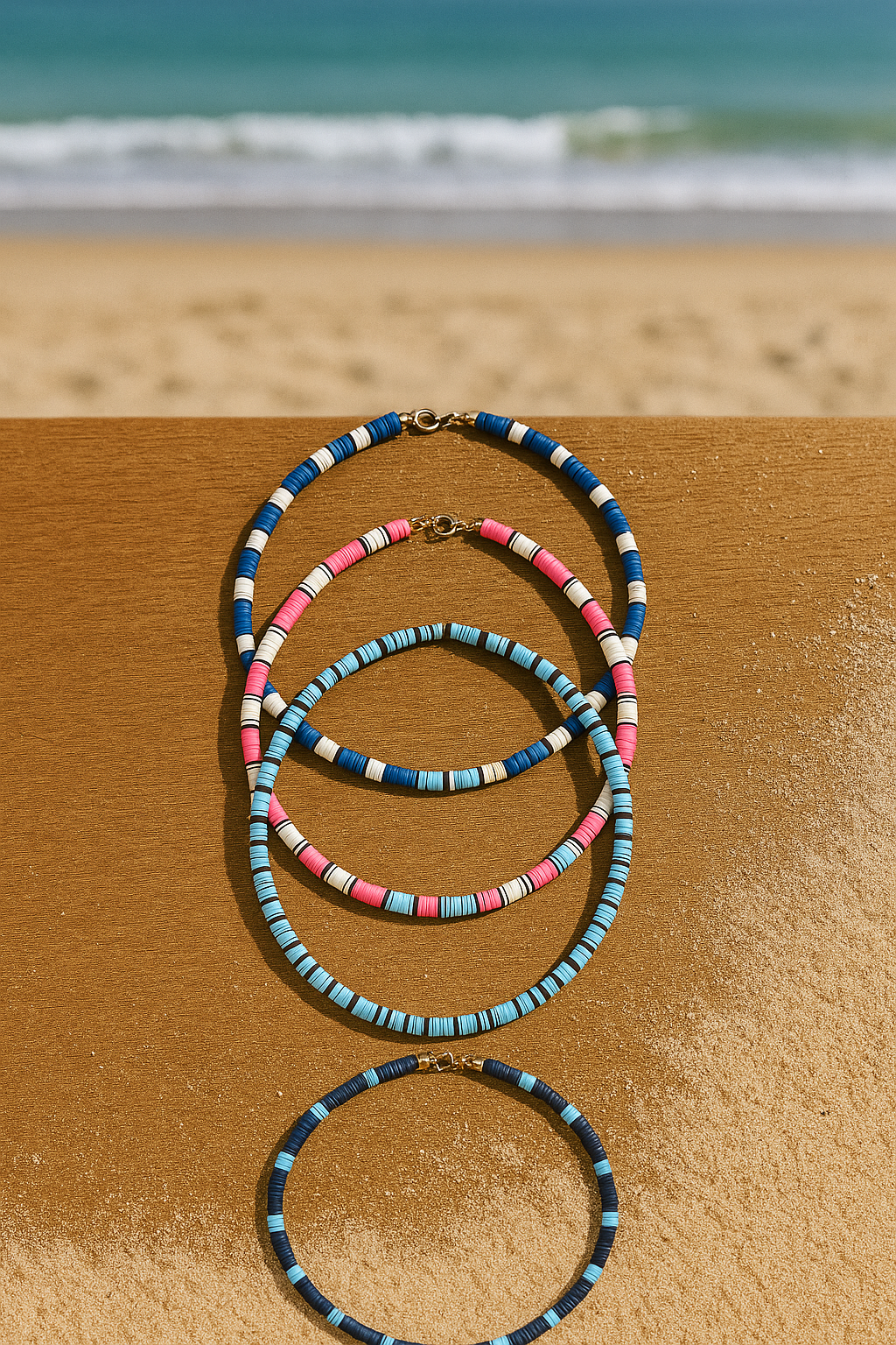 Colorful beaded bracelets stacked on sand with a blurred beach and ocean in the background