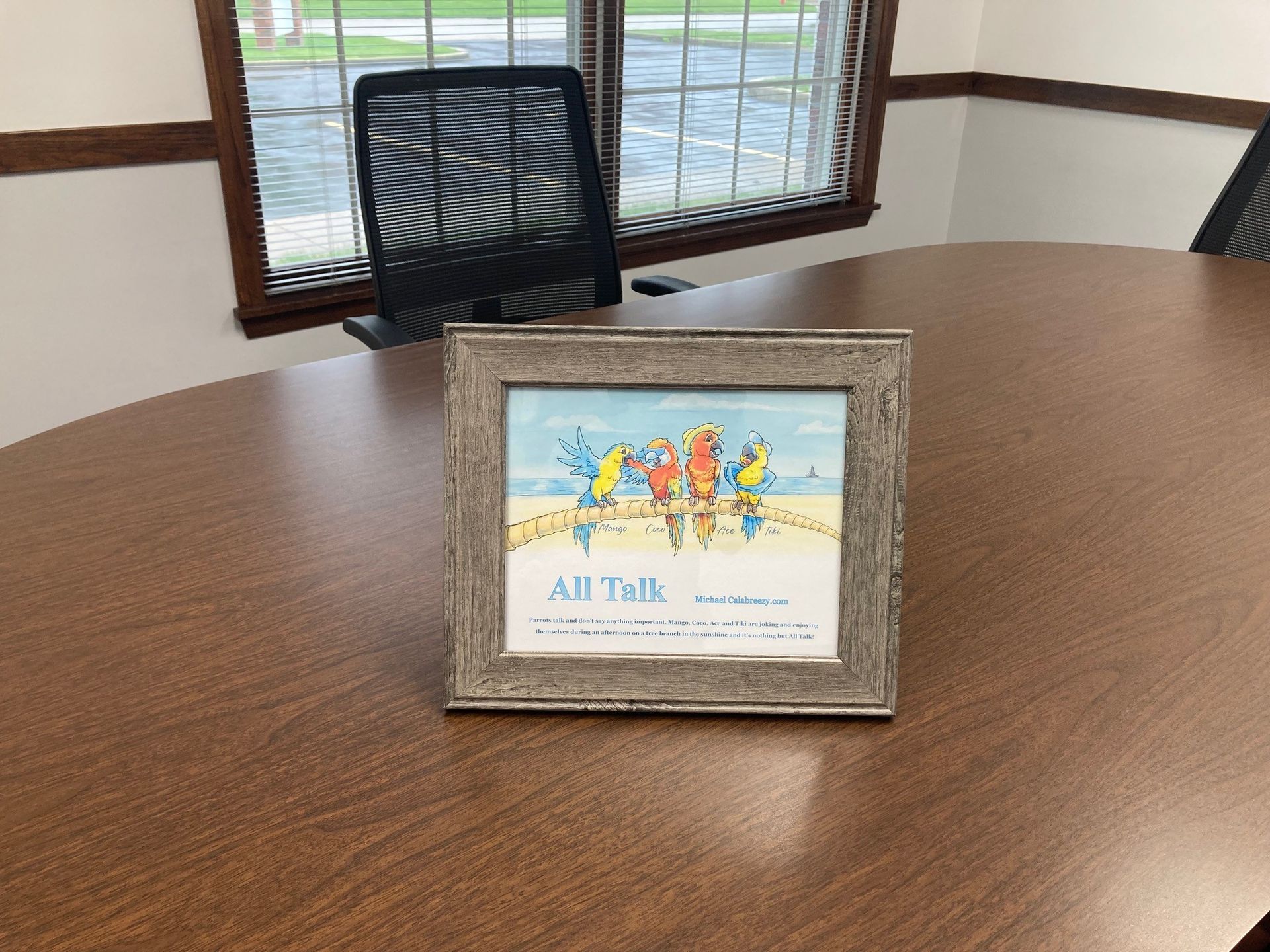 Framed “All Talk” sign on a wooden table in an office room with a chair and window behind it