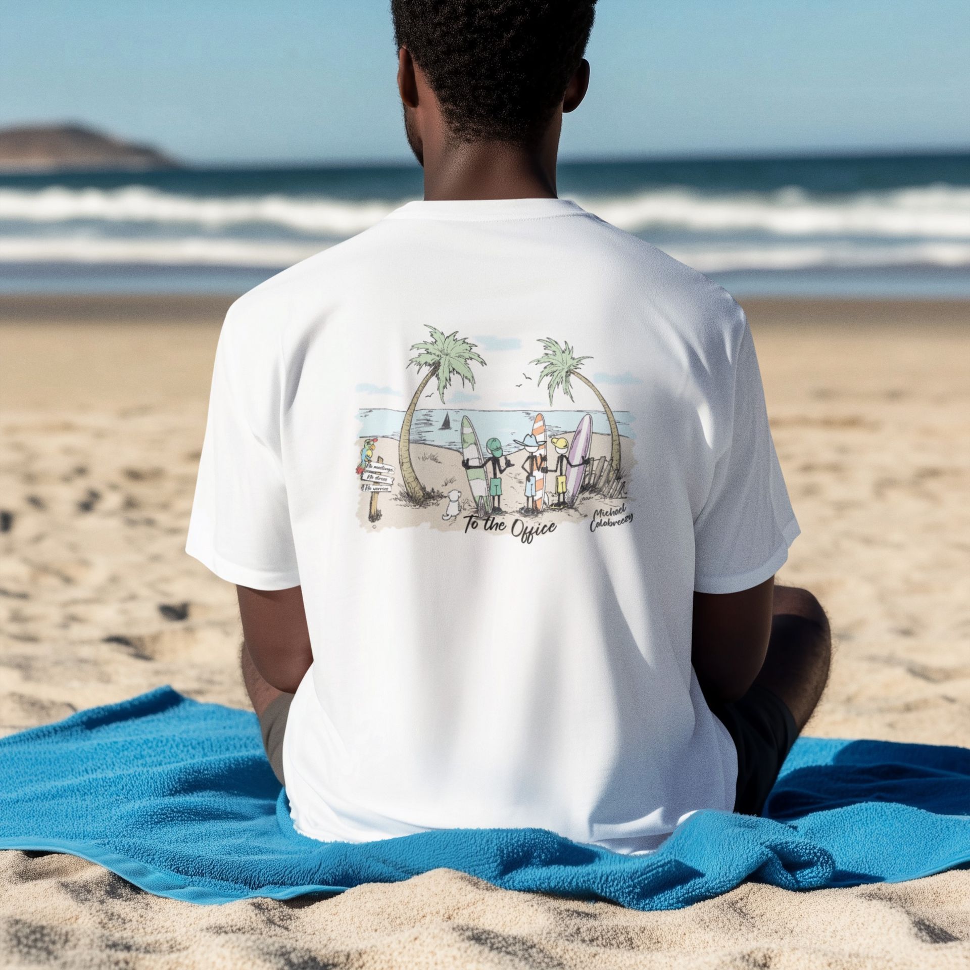 Person seated on a blue towel at the beach, wearing a white T-shirt with a coastal illustration on the back.