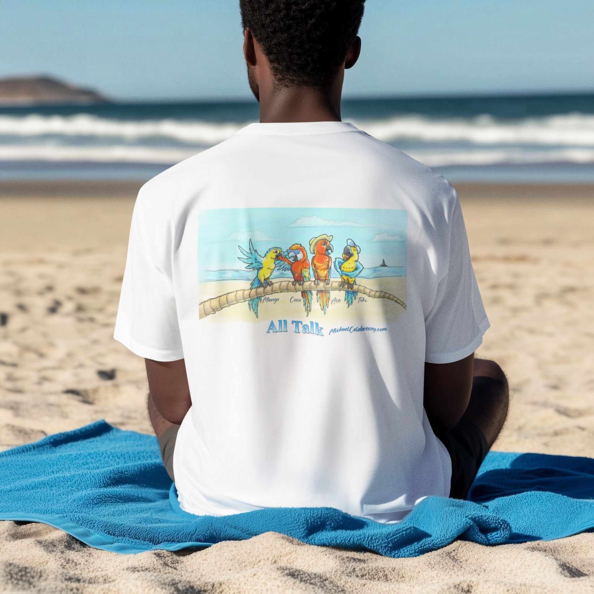 Person sitting on a beach towel, wearing a white T-shirt with a colorful graphic on the back.