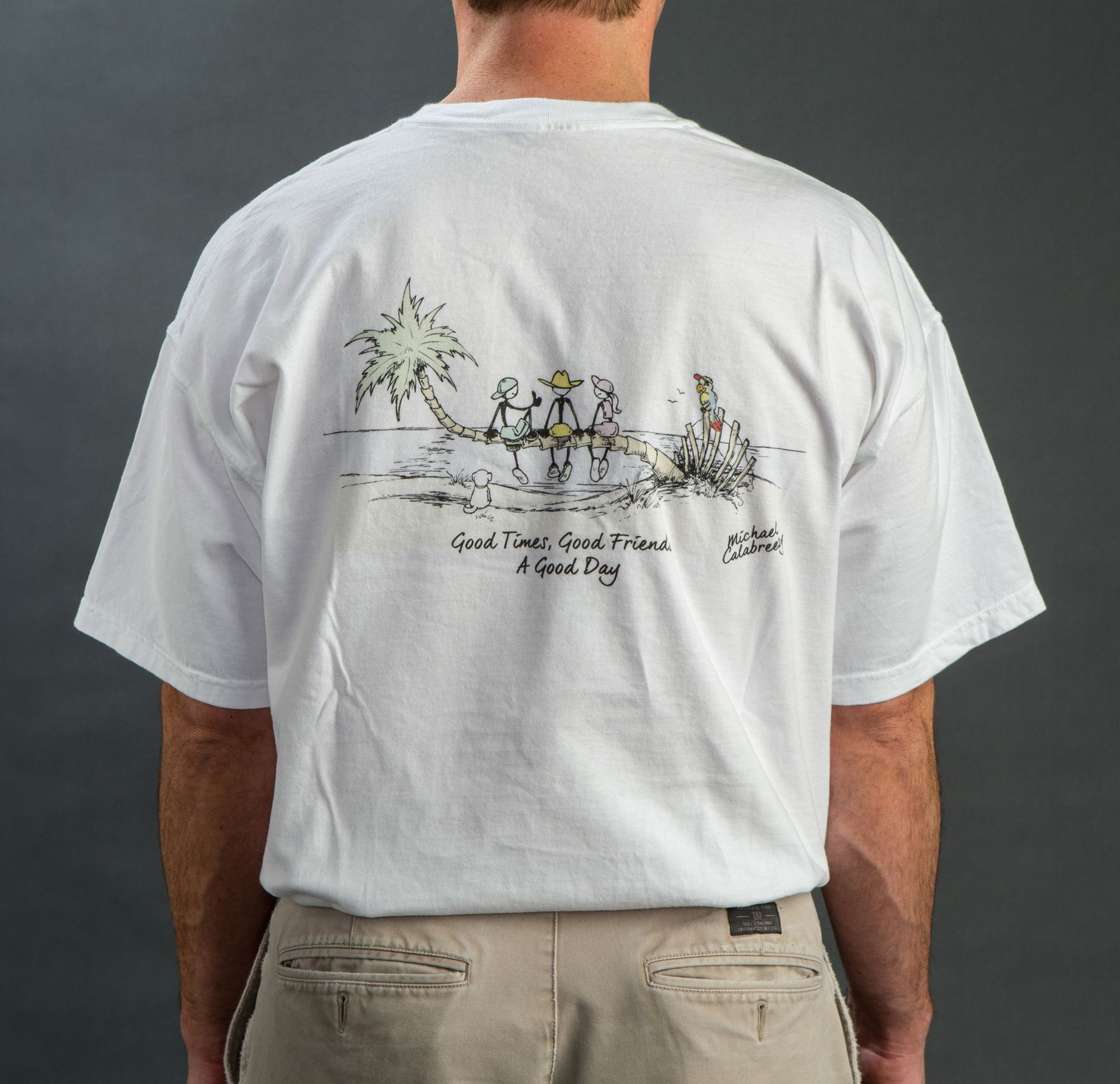 Man wearing a white graphic T-shirt with a beach-themed illustration on the back.