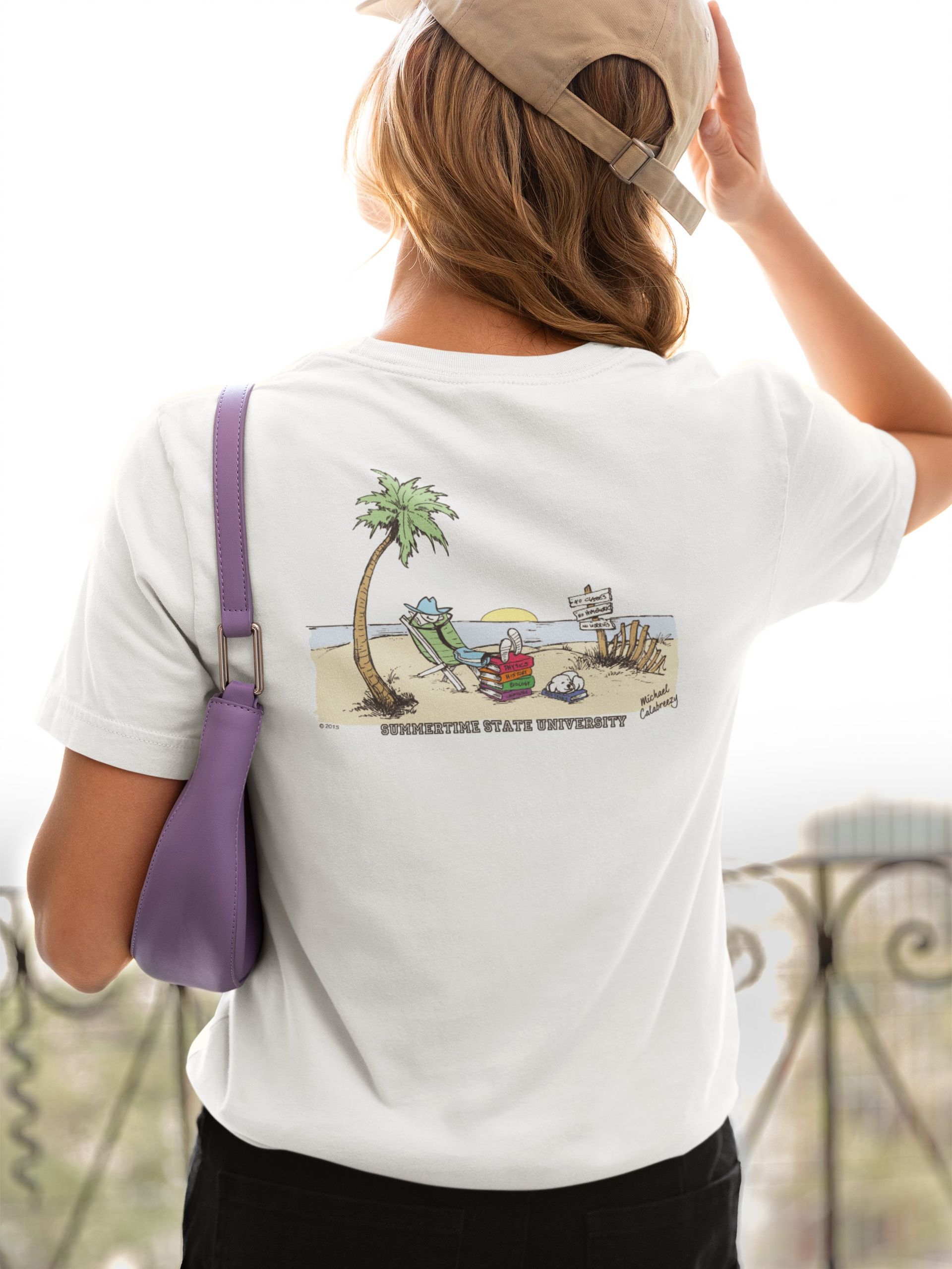 Person in white T-shirt and hat stands by a balcony, holding a purple bag and looking out over a view.