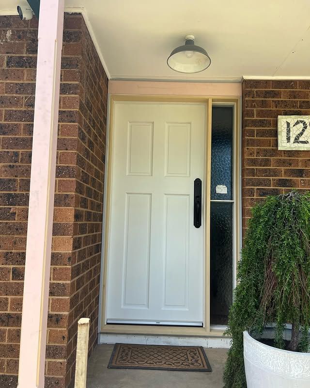 Front porch with white front door, brick walls, welcome mat, and house number 12.