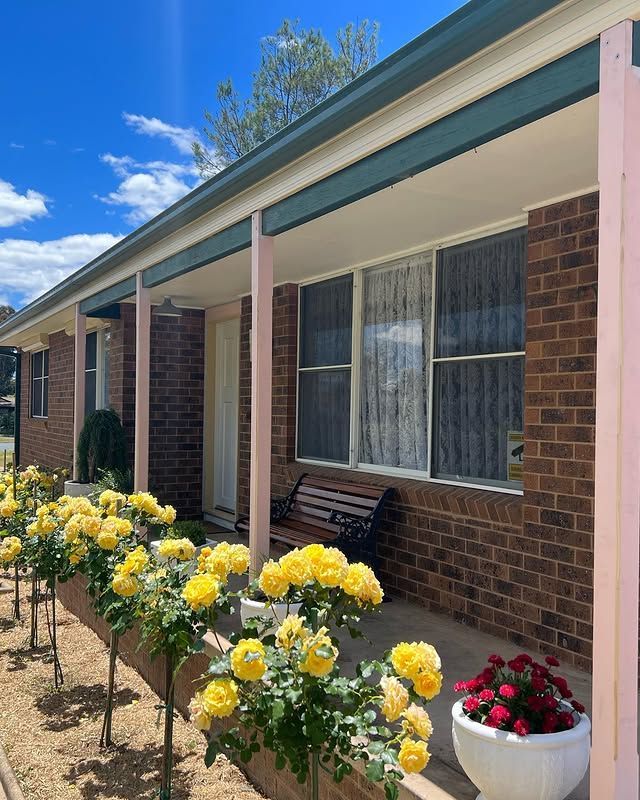 Brick house porch with yellow flowers in the garden and white-red potted blooms by the window