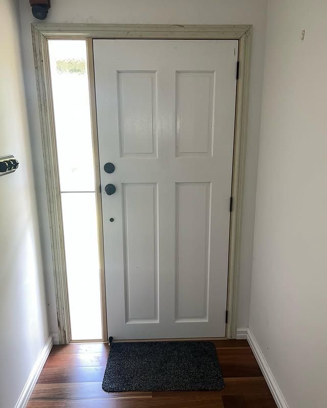 Front door with white panels and a small doormat, slightly open to bright light outside.