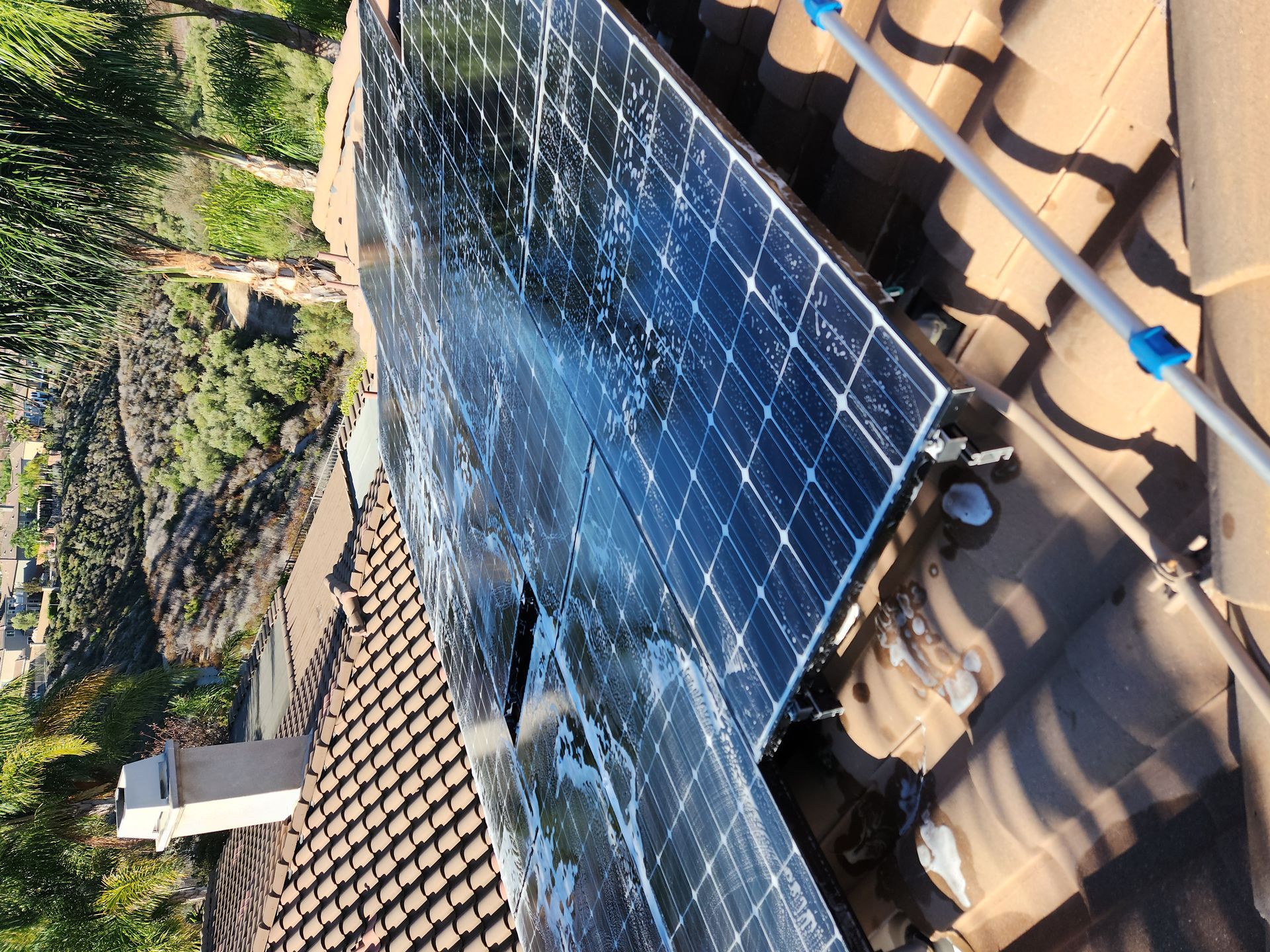 Solar panels mounted on a tiled roof beside a chimney, viewed at an angle