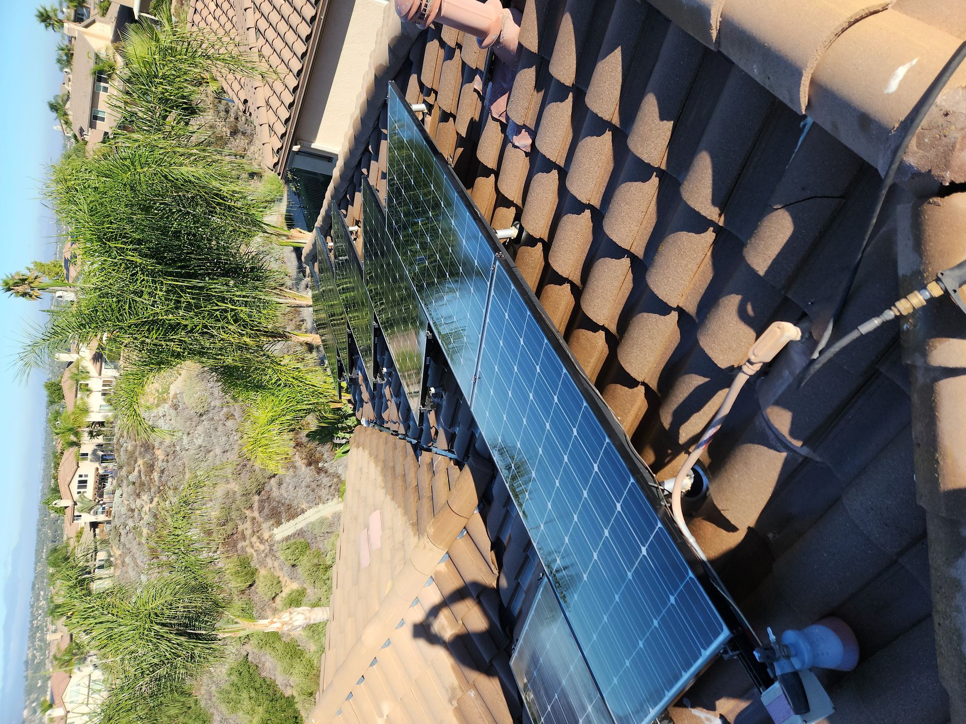 Solar panel mounted on a tiled rooftop beside a garden and distant water view.