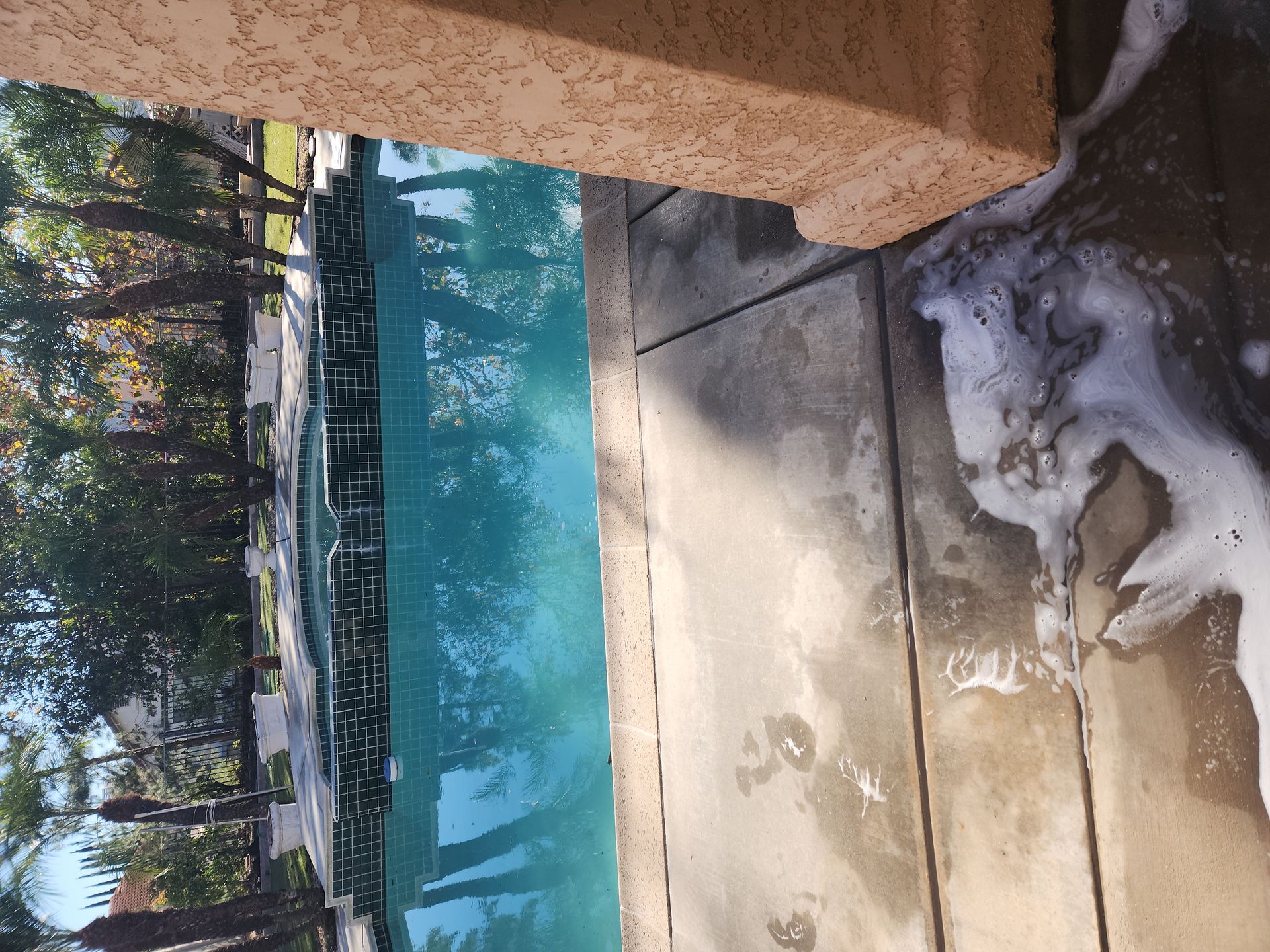 Snow beside a turquoise pool by a wooden deck, with trees reflected in the water.