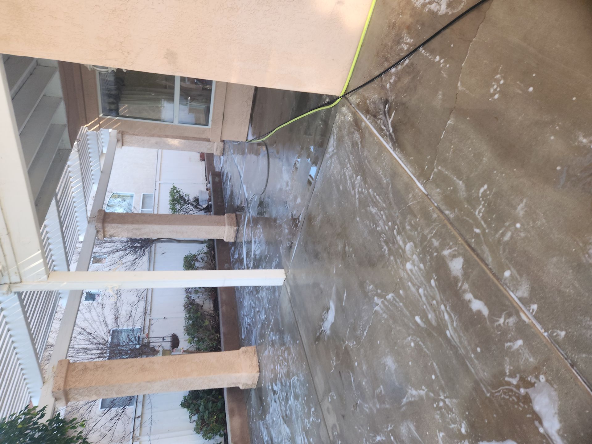 Covered outdoor walkway with white pillars and wet concrete ground beside a building