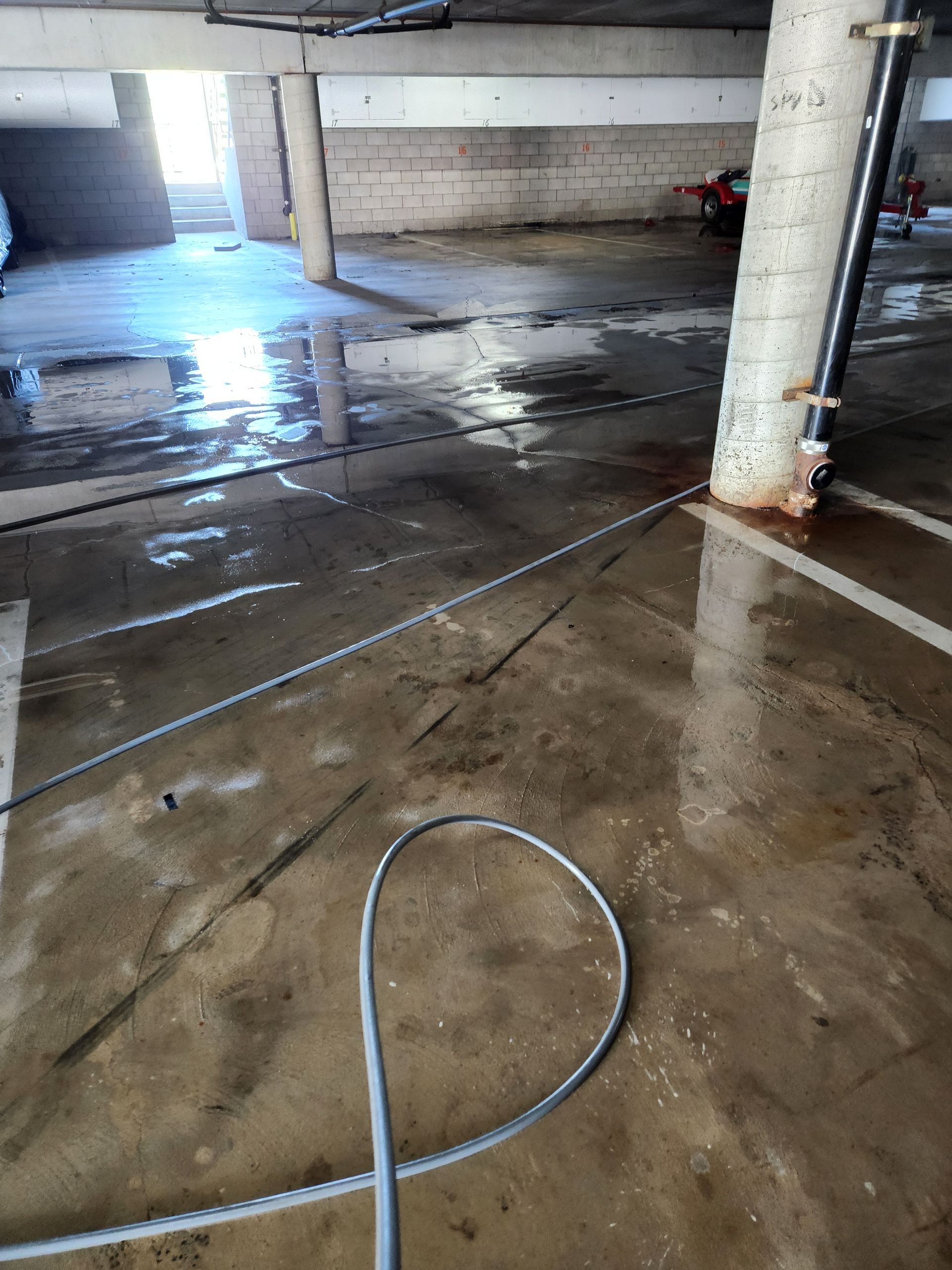 Wet concrete floor in a parking garage with a hose and pillar reflections on the slick surface
