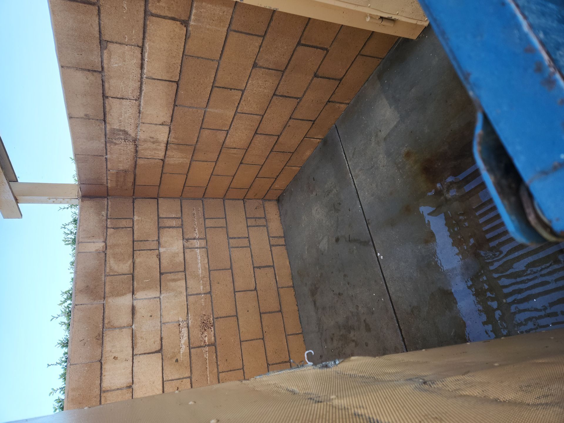 Brick patio and wall beside a wet concrete floor, viewed at an angle with a blue door frame.