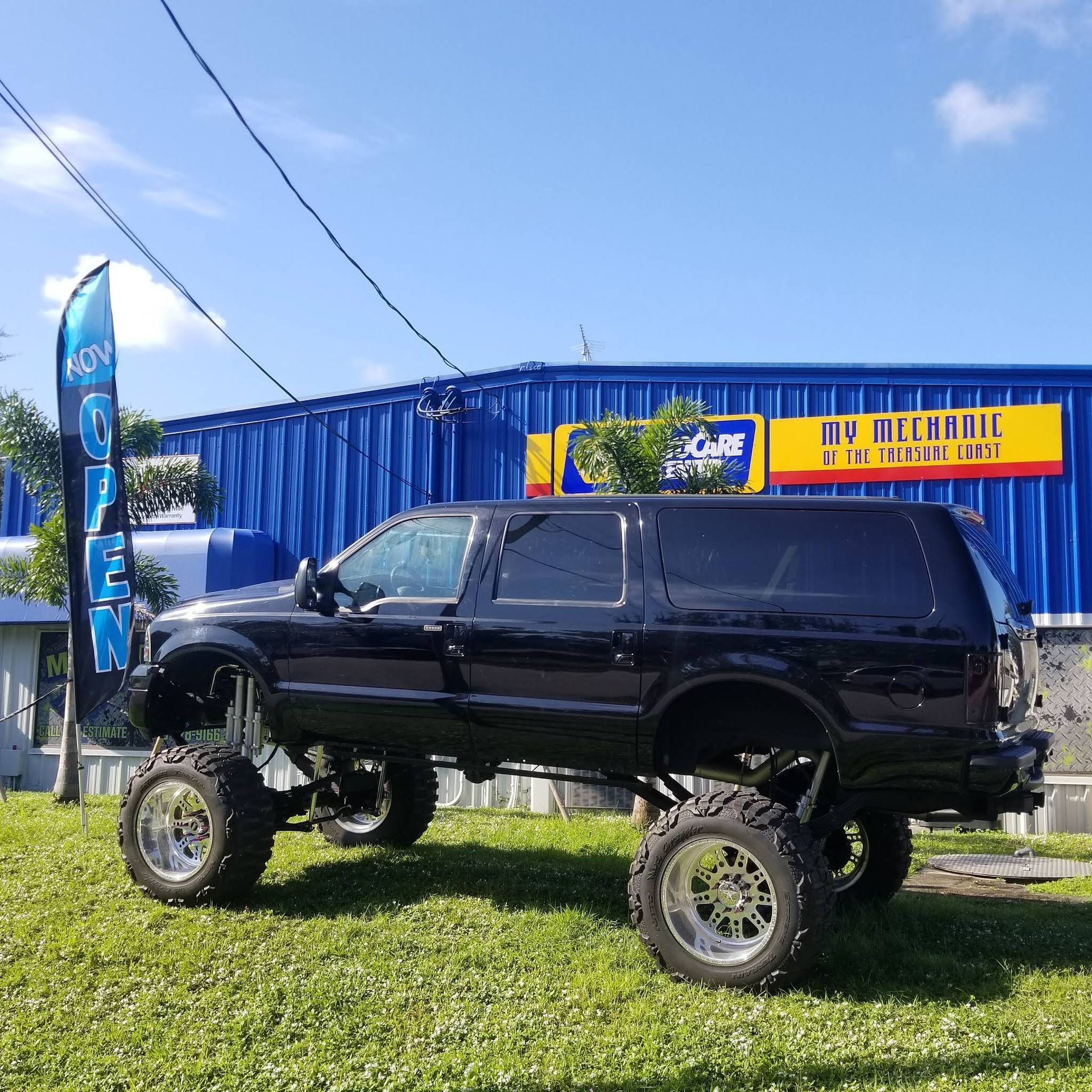A black lifted SUV parked on a grassy lawn in front of a blue industrial building with an