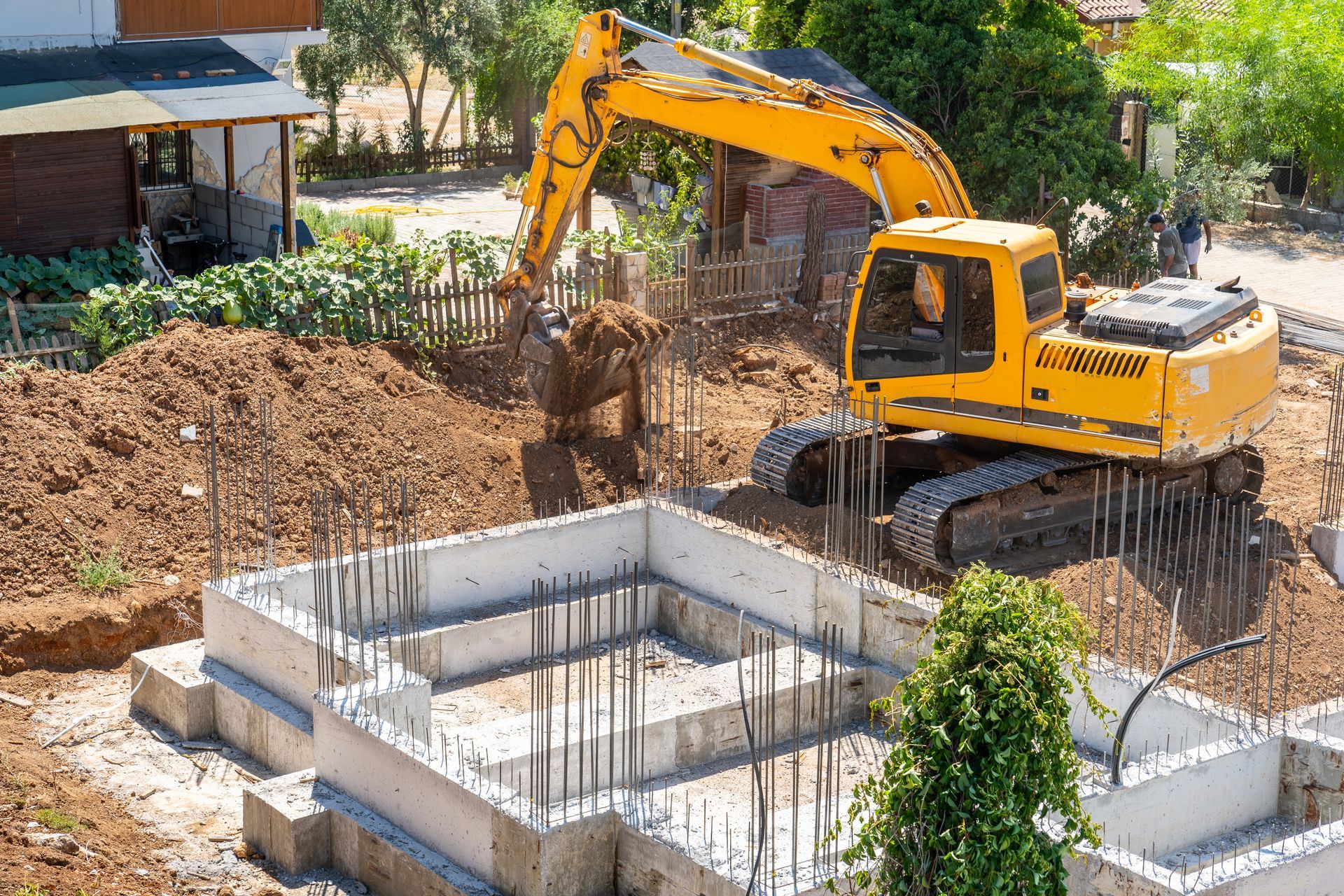 A yellow excavator is digging a foundation for a house.
