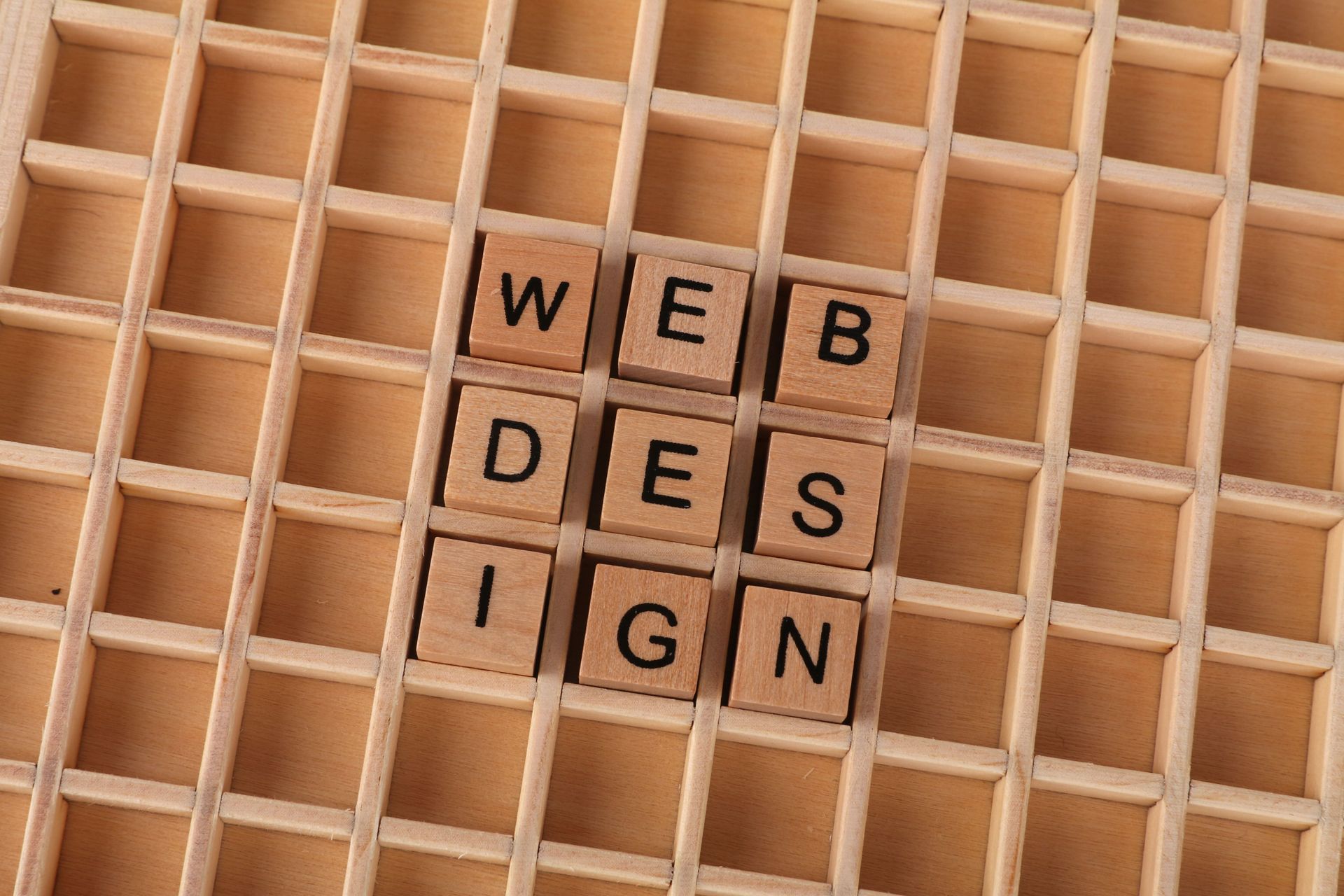 Scrabble tiles spelling “WED DES IGN” on a wooden grid board