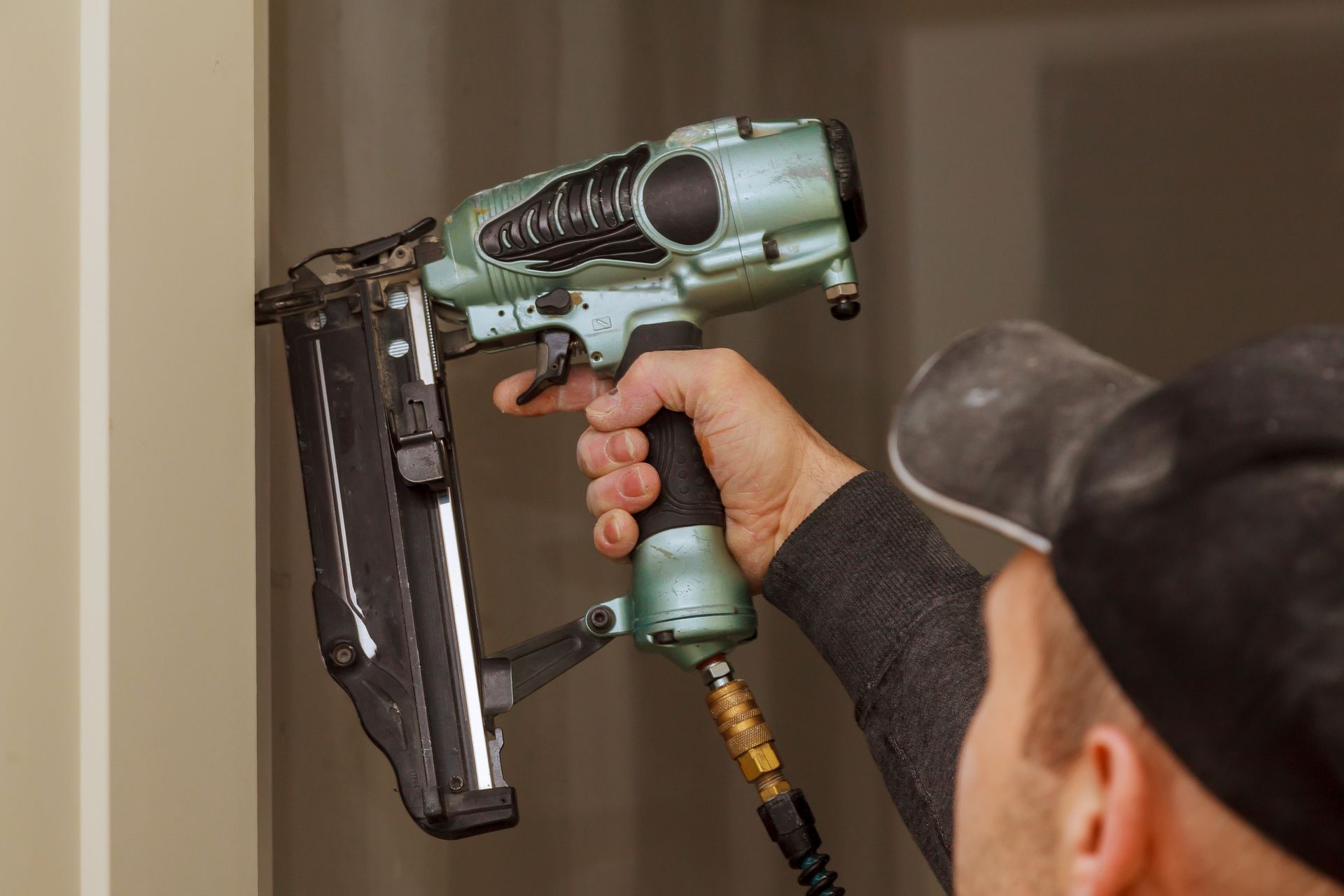 Persona che utilizza una pistola pneumatico verde per fissare le modanature in interni.