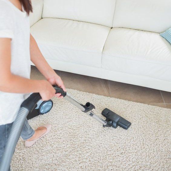 A woman is vacuuming a carpet in a living room