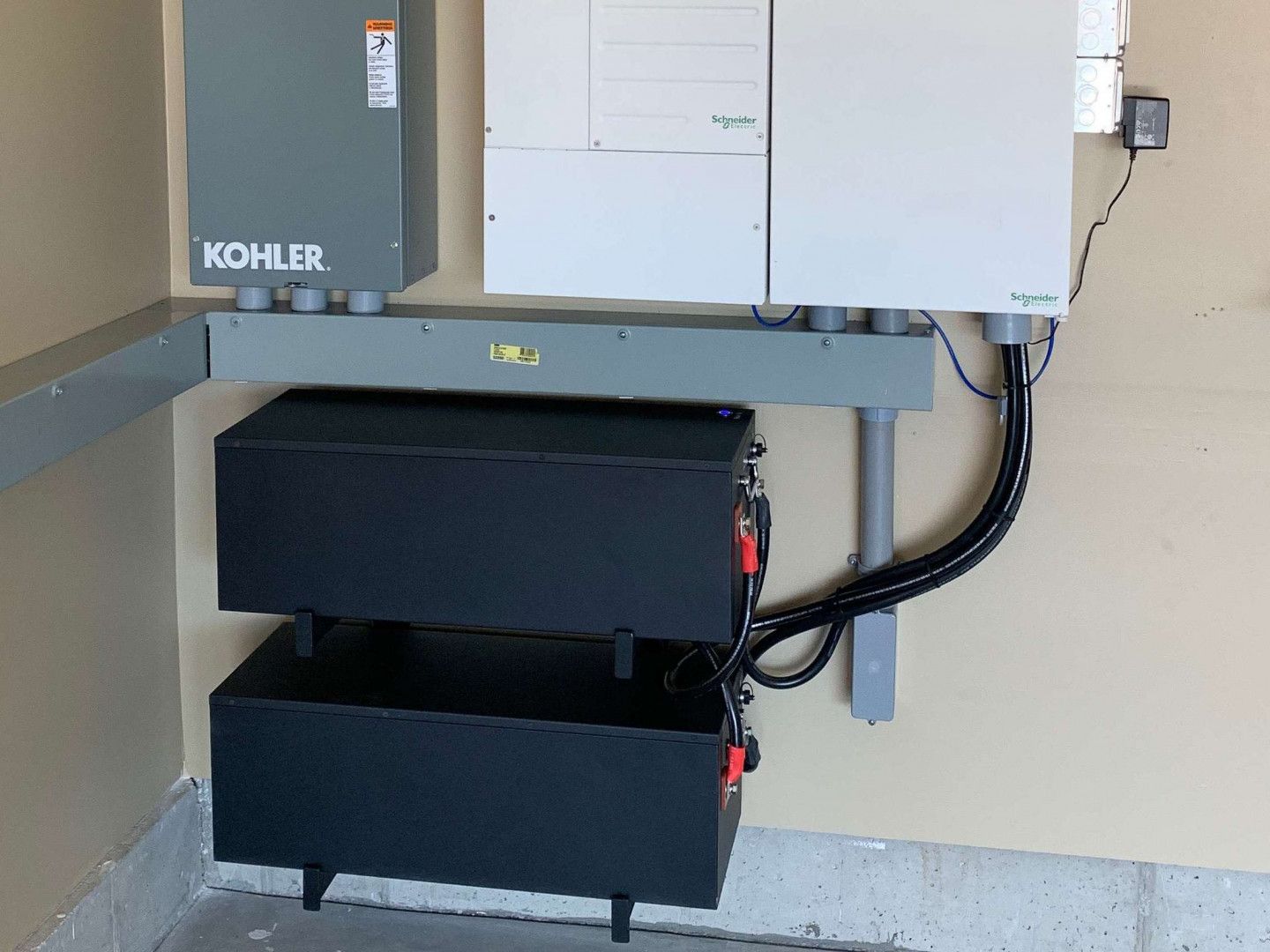 Solar battery backup system with two black storage units, mounted on a wall with gray Kohler box and electrical components.