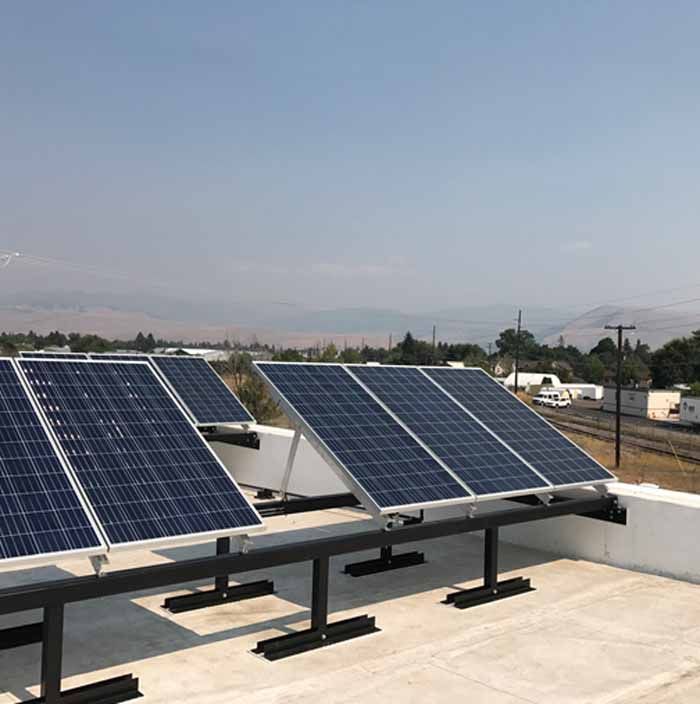Solar panels on a flat roof, angled towards the sky, with a distant landscape visible.