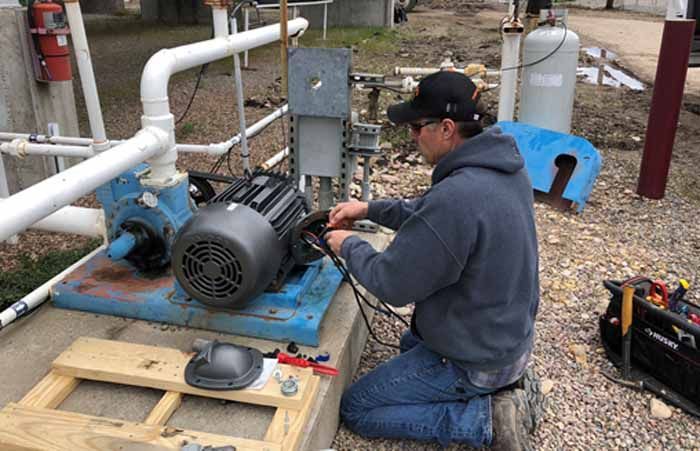 A technician works on the wiring of an electric pump motor at an outdoor industrial site.