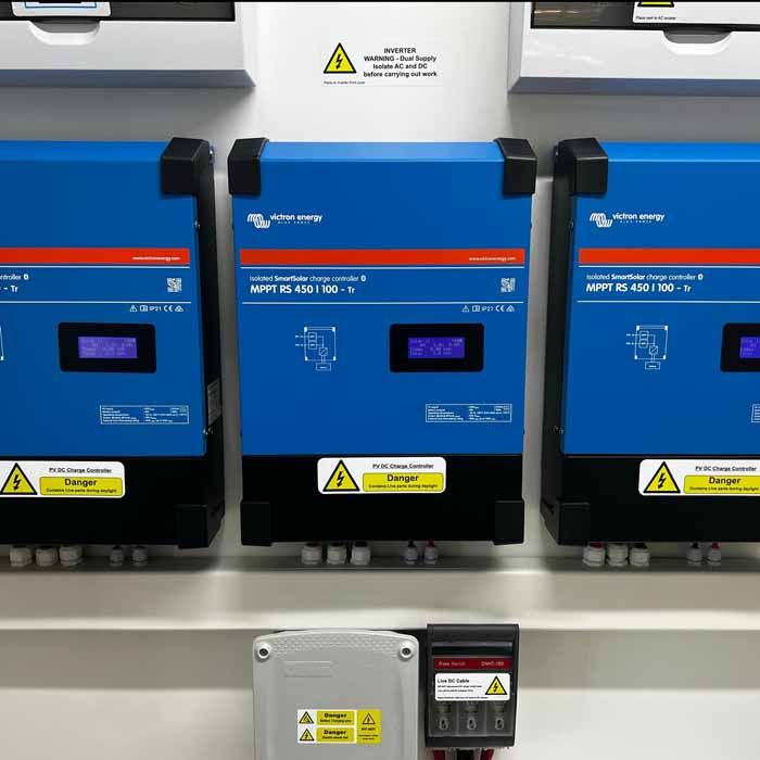 Three blue solar inverters mounted on a wall with warning labels and digital displays.