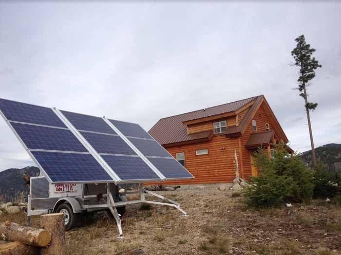 Solar panel array next to a wooden cabin on a hillside, with a cloudy sky.