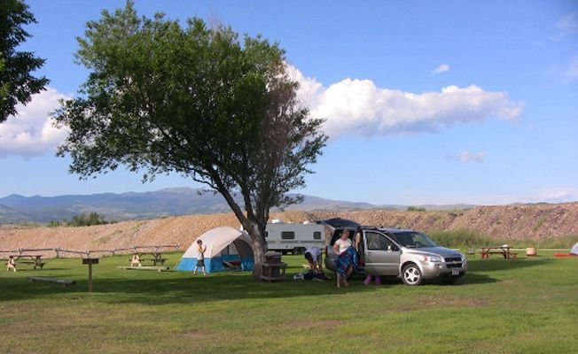 A car is parked in a grassy field next to a tent.