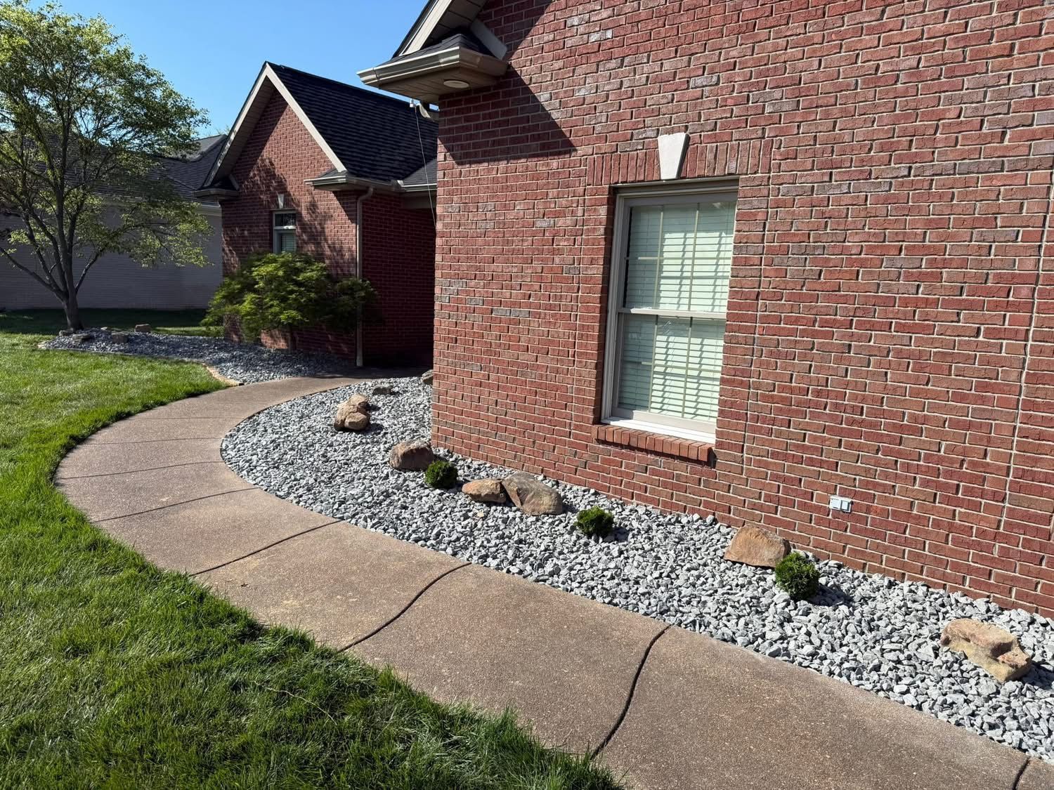 Brick house exterior with curved concrete walkway and gravel flower bed along the wall