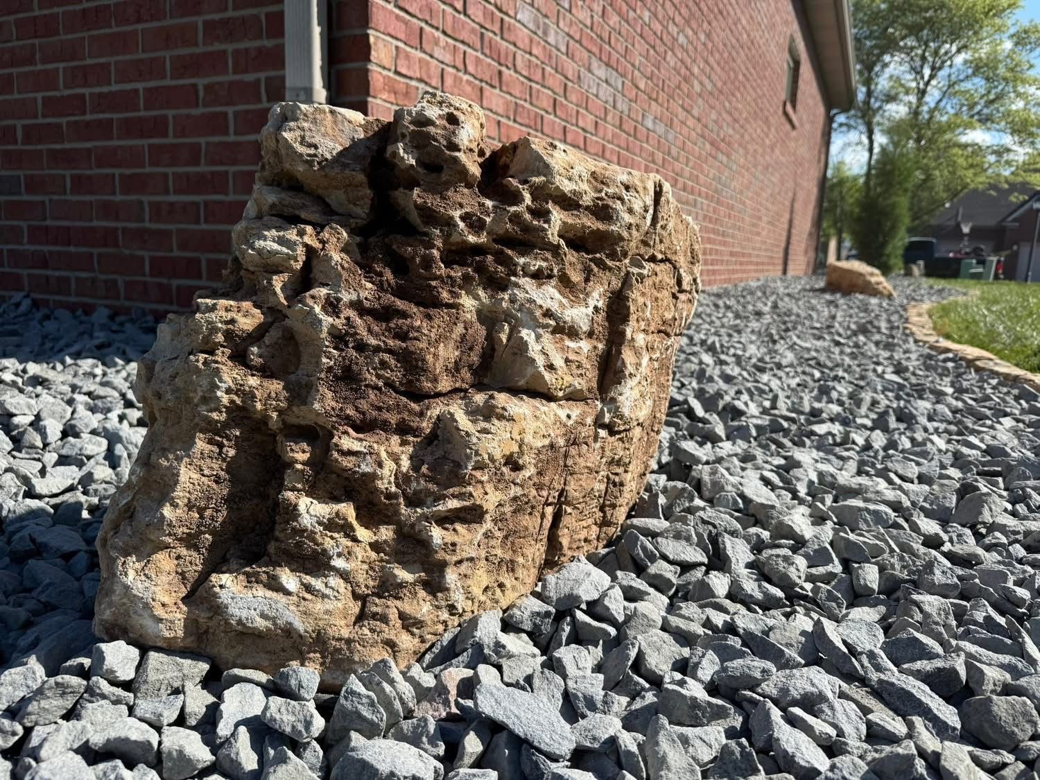 Crumbled tan brick foundation beside a red brick wall on gray gravel landscaping