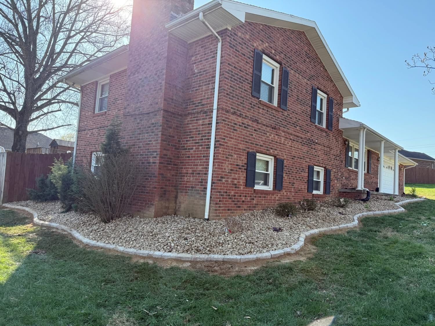 Brick house exterior with white trim, blue shutters, and a sunlit front yard