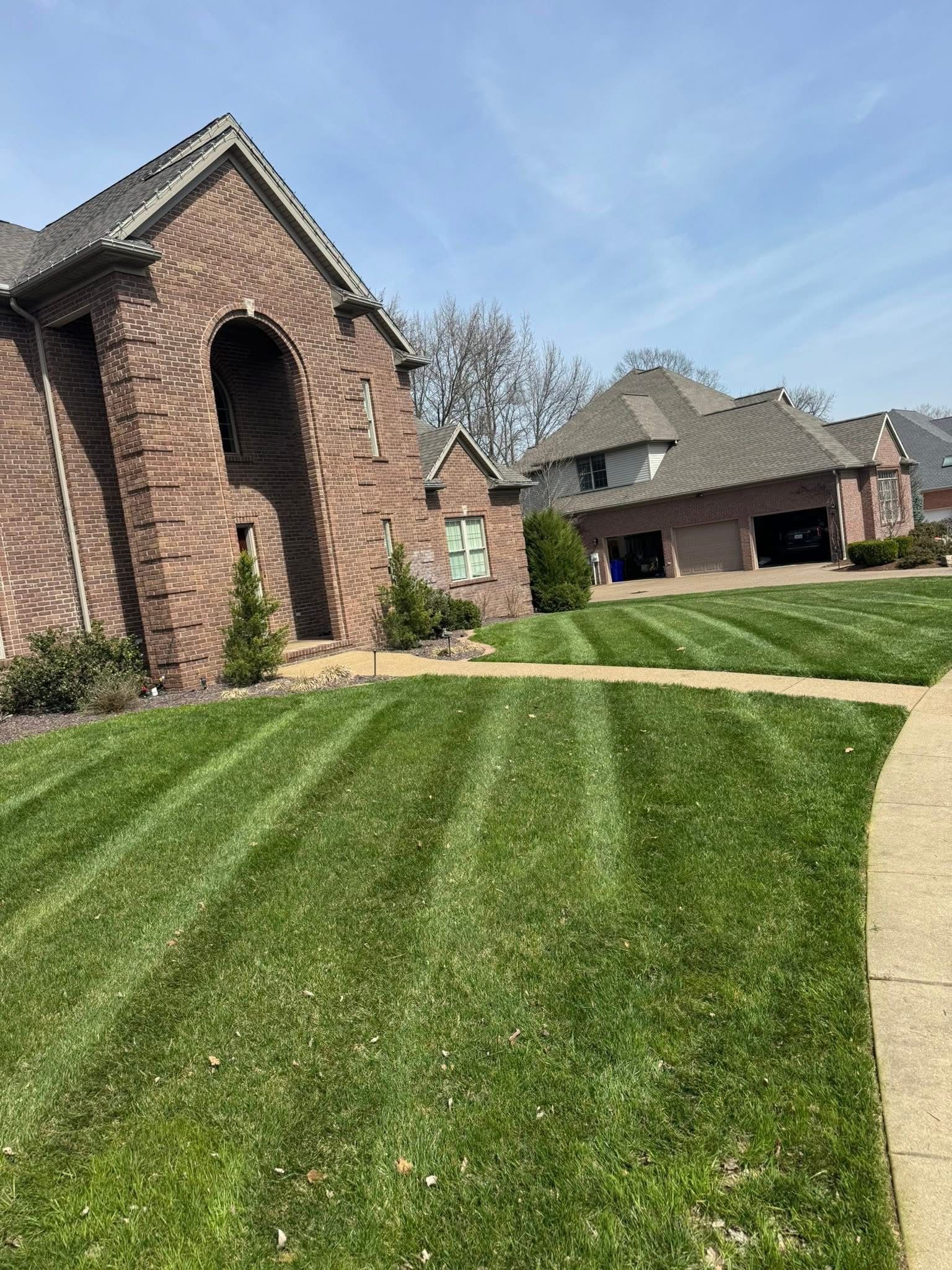 Brick house with arched entry, striped green lawn, and driveway beside a detached garage under a blue sky