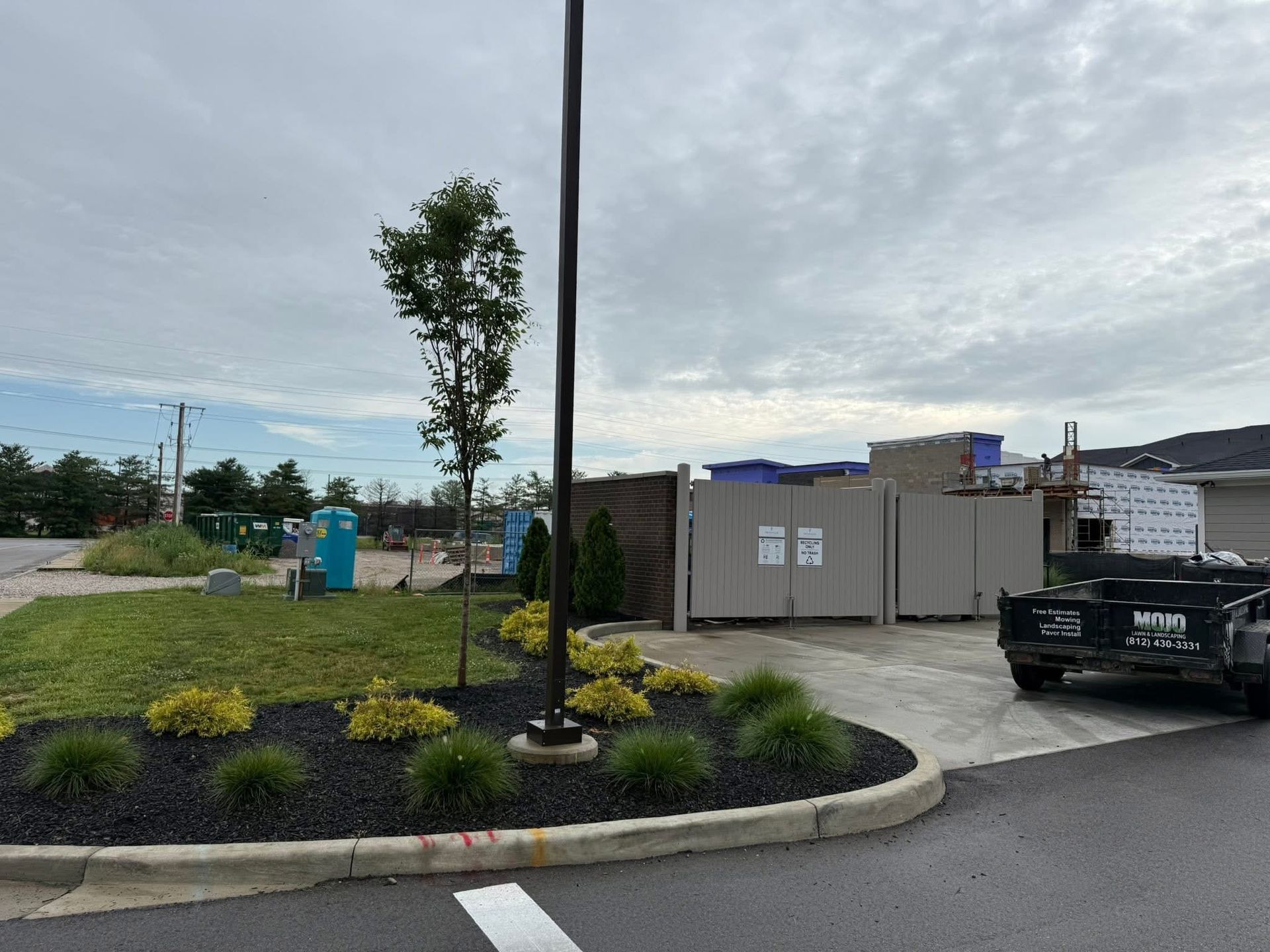 Parking lot with a black pickup, utility buildings, lamp post, and landscaped curb under a cloudy sky