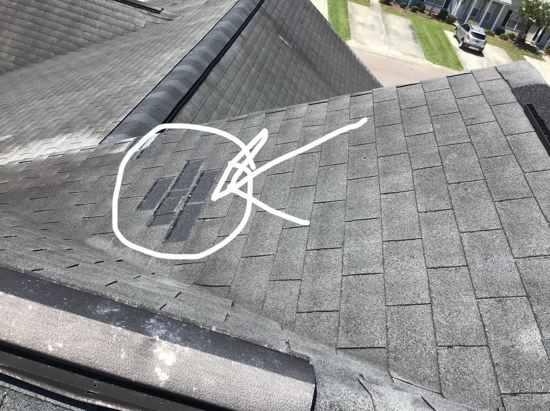 Close-up of a dark asphalt shingle roof. White circle highlights several missing shingles near a roof peak.