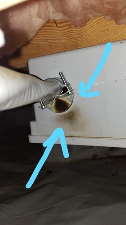 Plumber inspecting sink pipes, holding a clipboard and wrench. He wears a cap and jeans.
