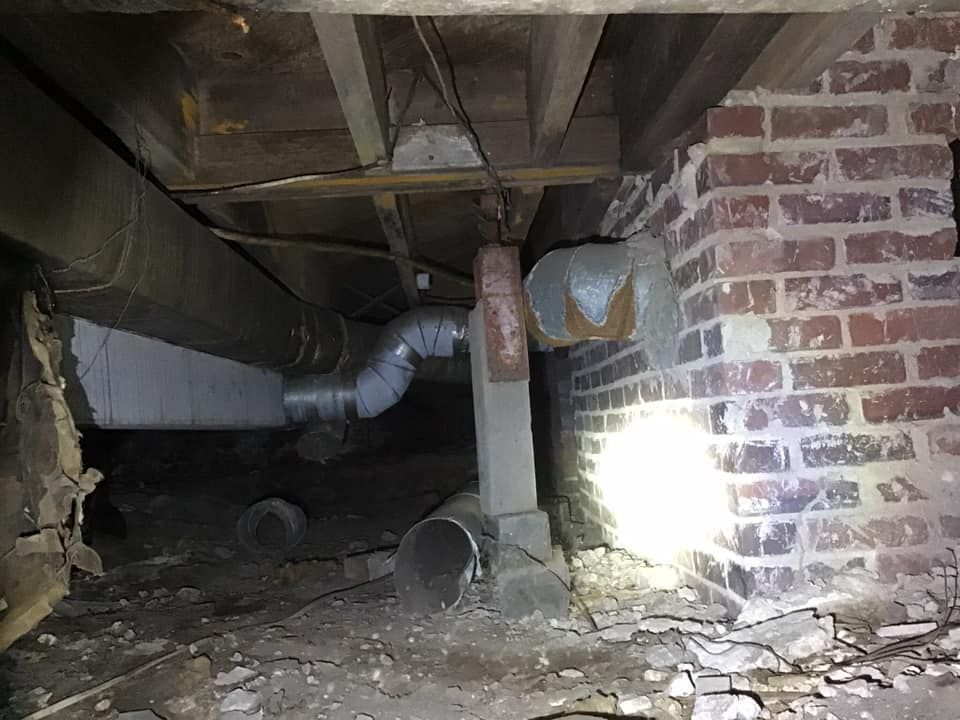 Underneath a house: ductwork and brick foundation visible with flashlight. Dark, cramped space.