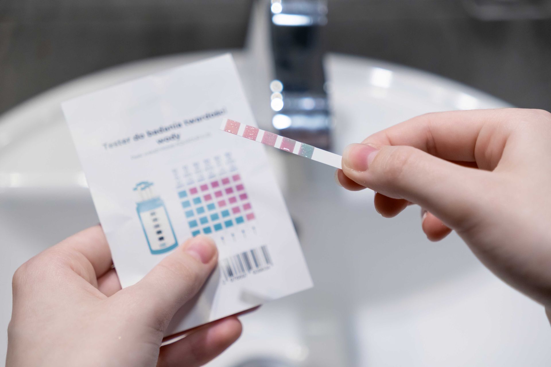 Person holding a urine test strip and its color chart in front of a bathroom sink.