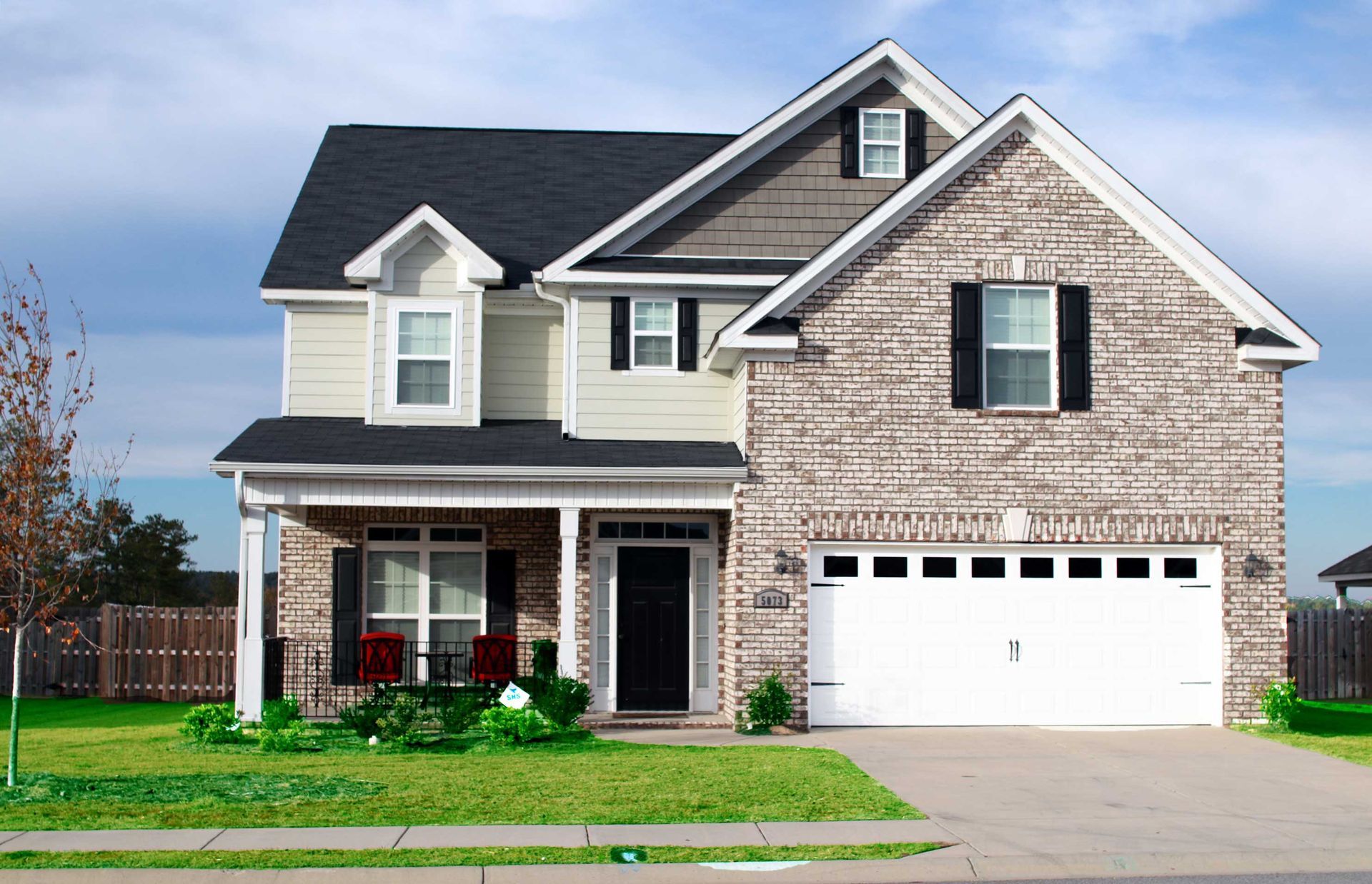 Two-story house with brick and siding exterior, black roof, white garage door, and green lawn.