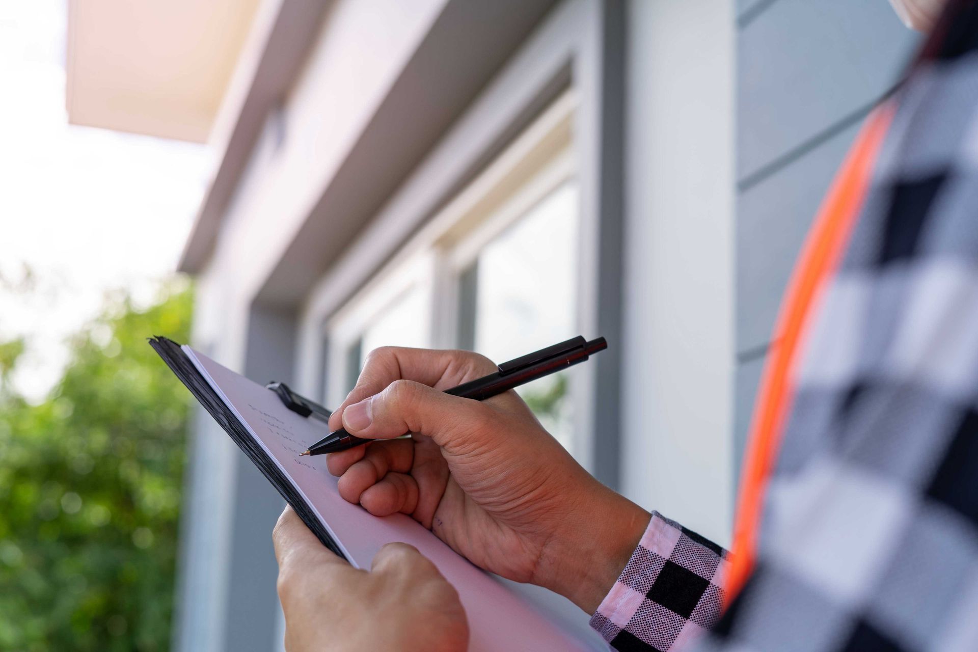 Person writing on clipboard next to a house; checking details.