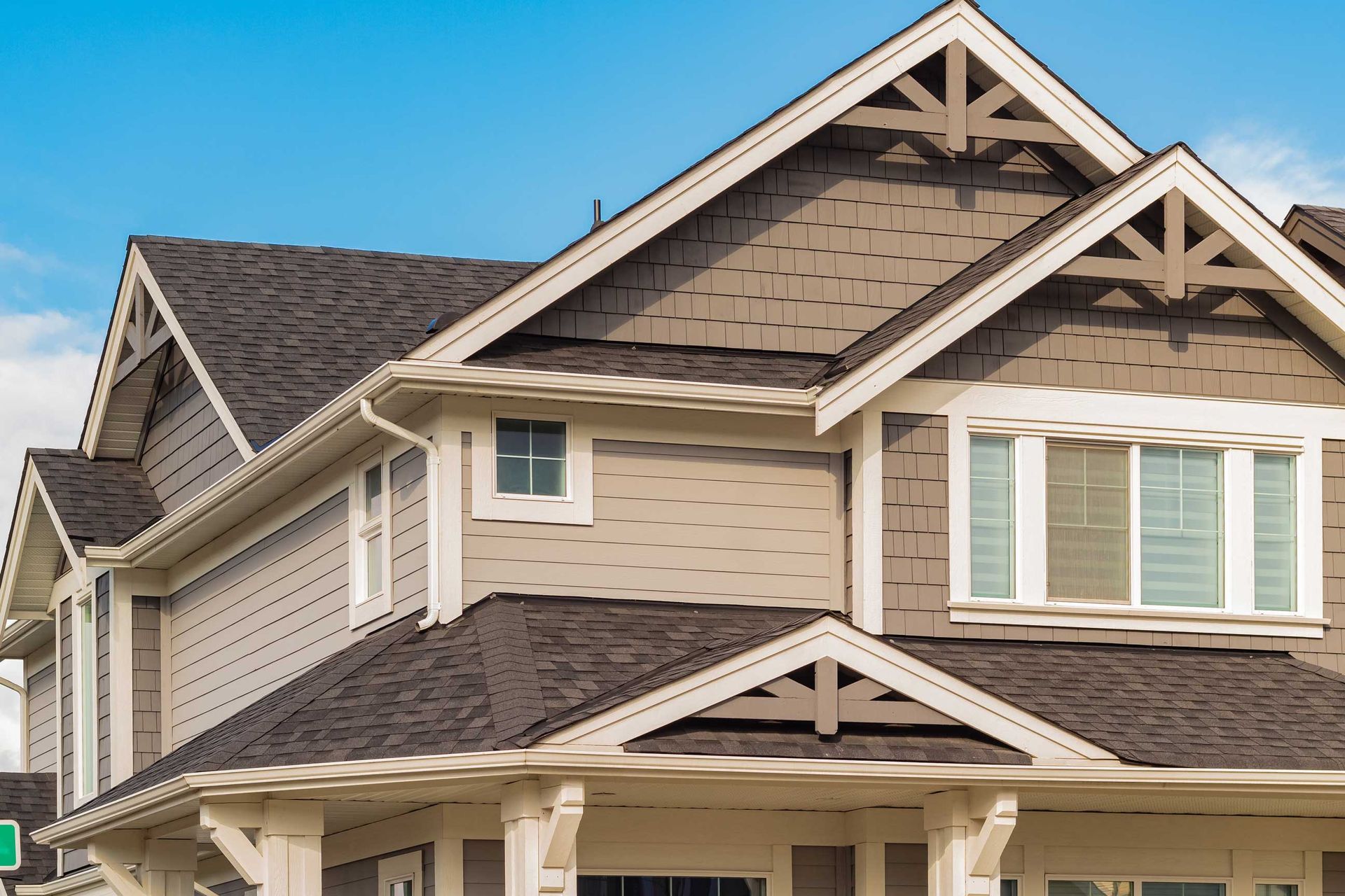 Two-story house with gray siding, dark roof, and white trim against a blue sky.